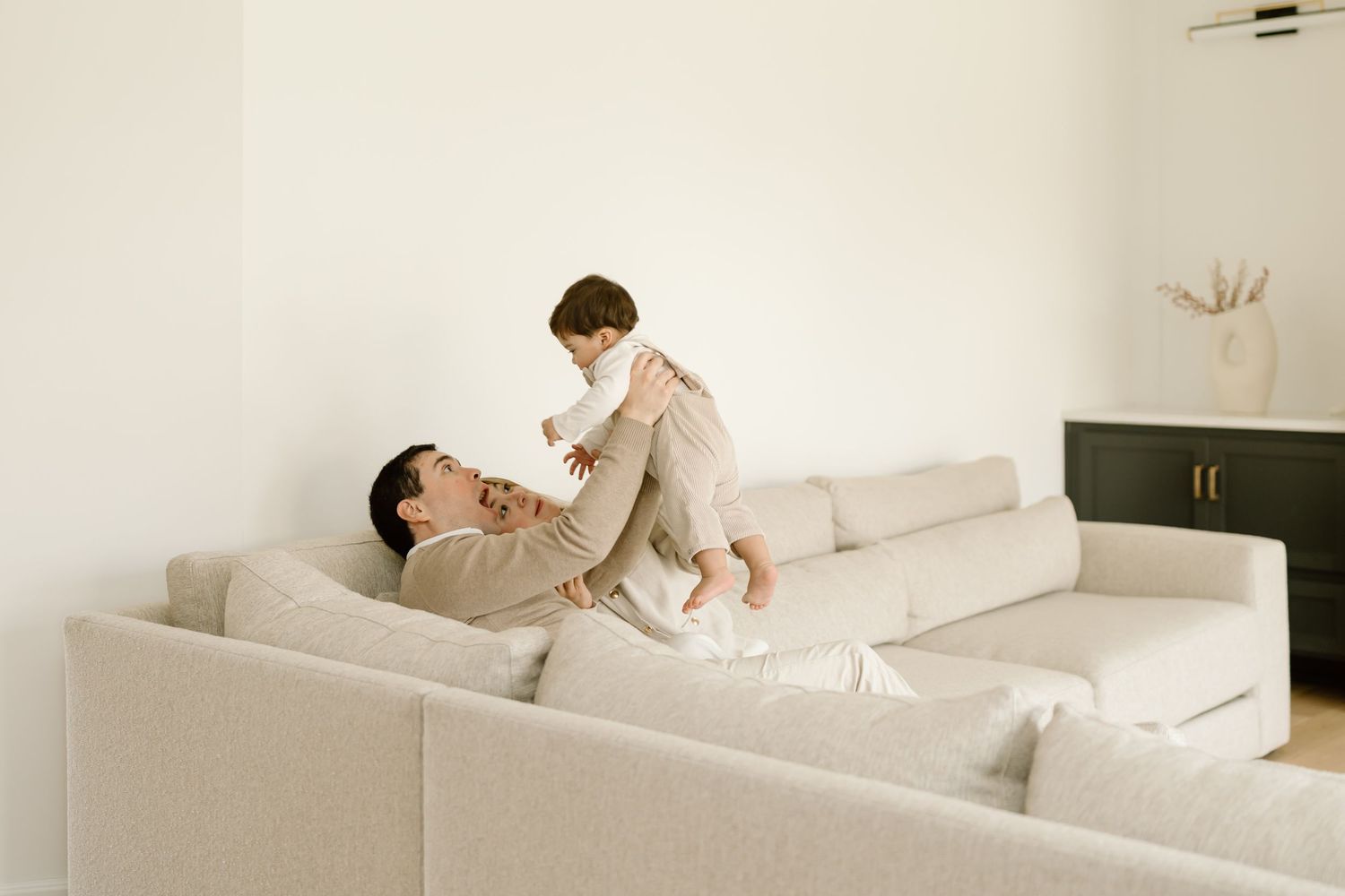 Parent and child share a playful moment together on a white modern sofa in a minimalist living room.