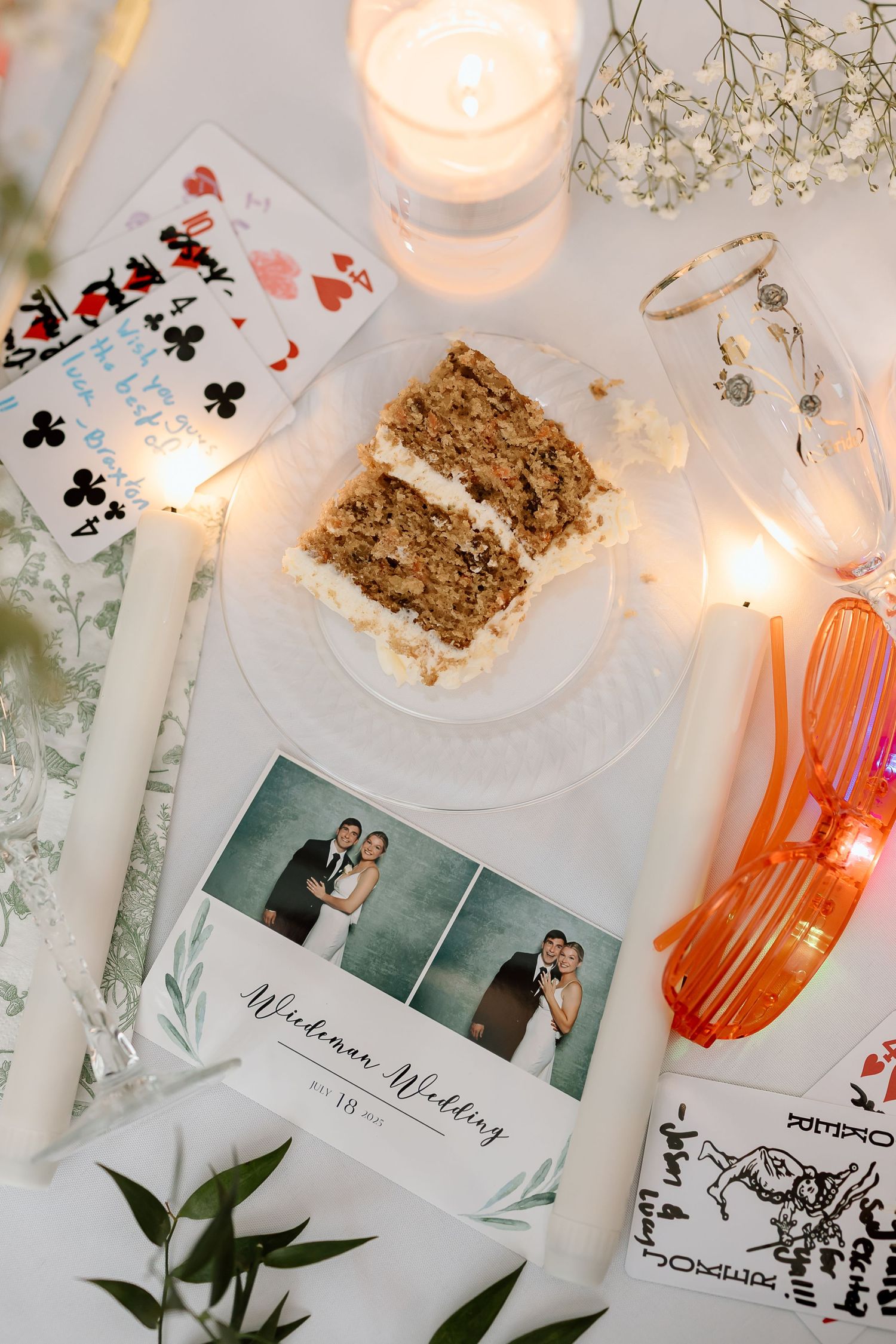 Elegant wedding reception table details with candlelight, photos, playing cards, and granola bars on white linens.