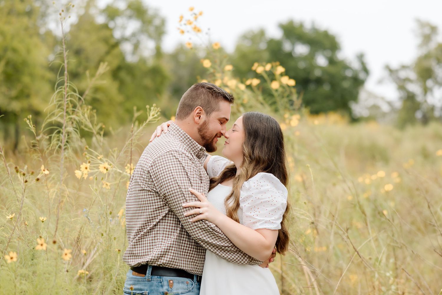 Two people share a tender embrace among golden wildflowers in a rustic outdoor setting.