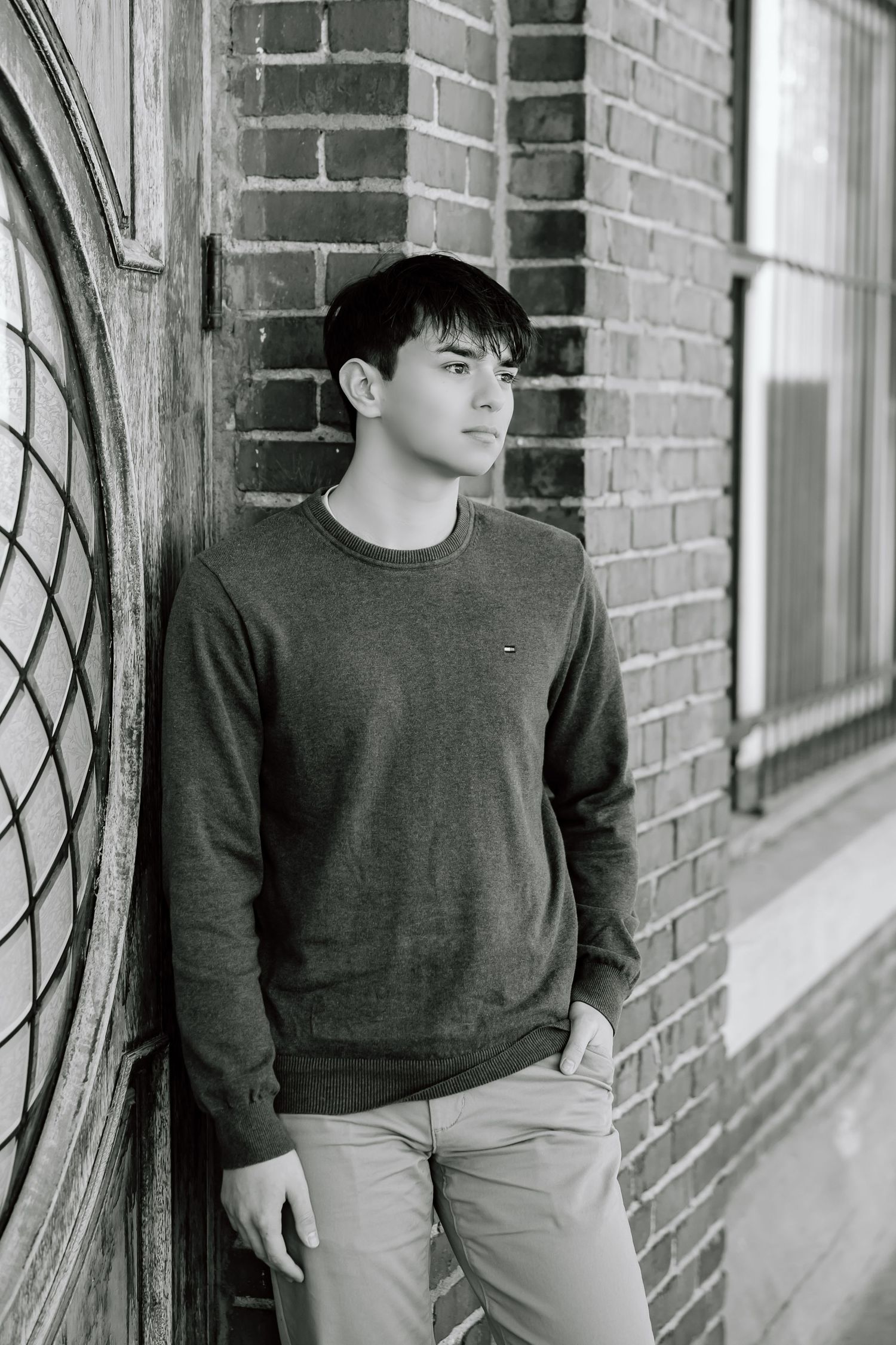 Portrait in a black sweater against brick wall with arched window.