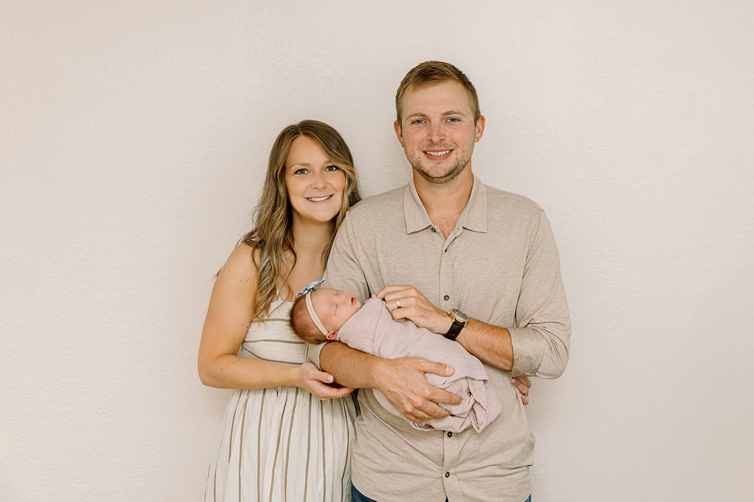 Family portrait against neutral backdrop with newborn in soft beige and cream tones.