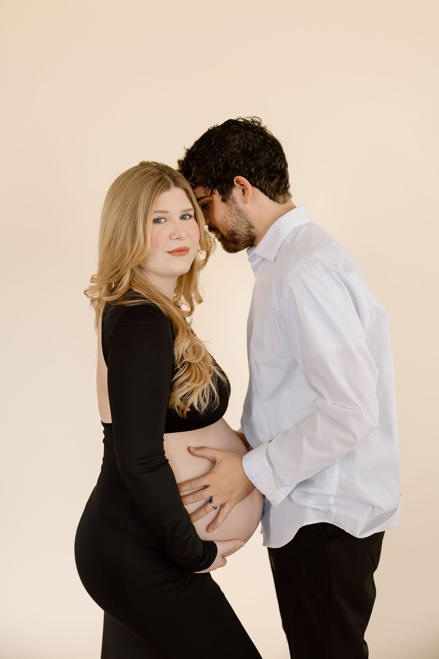 Romantic maternity photo with couple in black and white outfits embracing against beige backdrop.