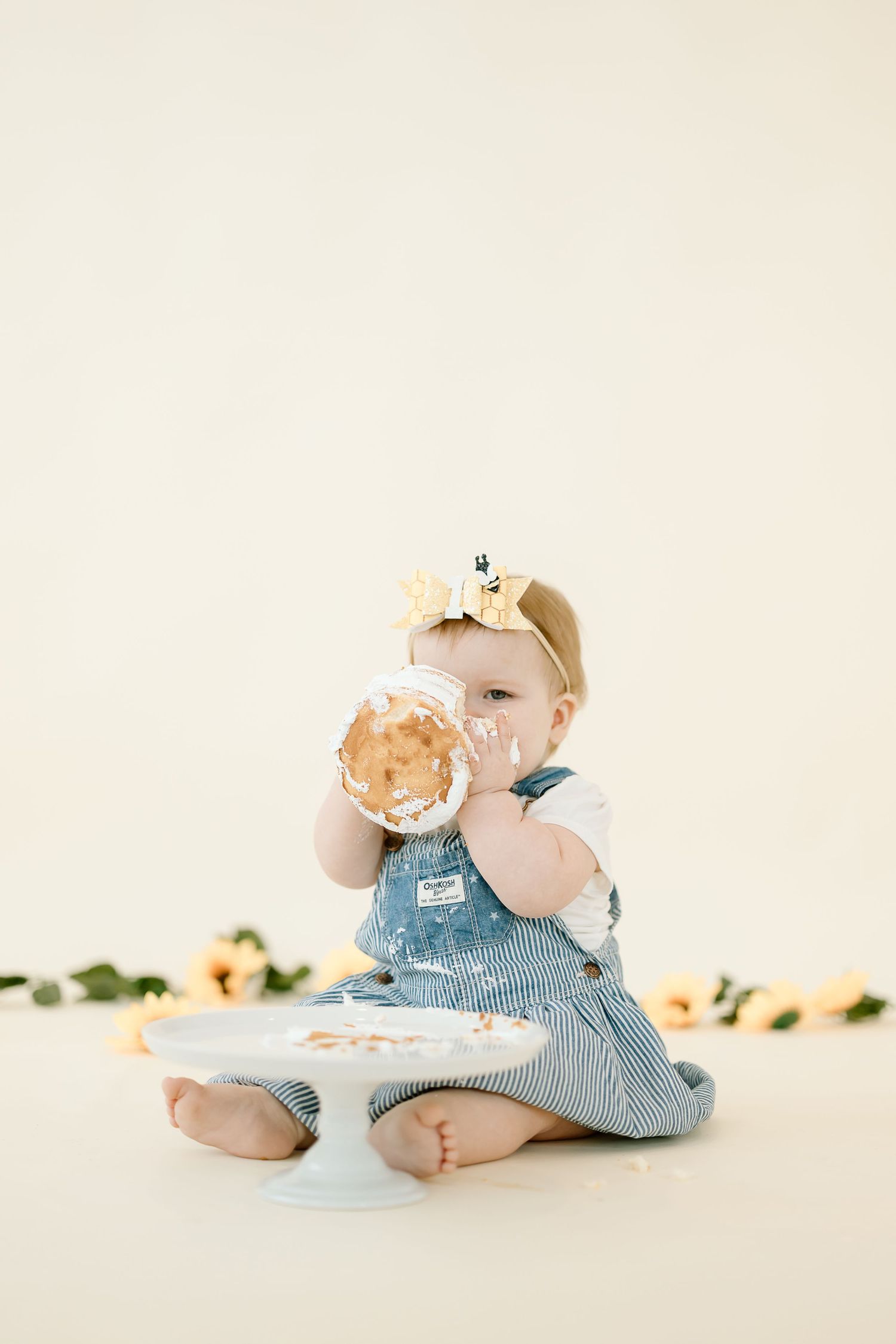 Baby in blue striped outfit sits on white background while playing with cake during first birthday cake smash photo session.