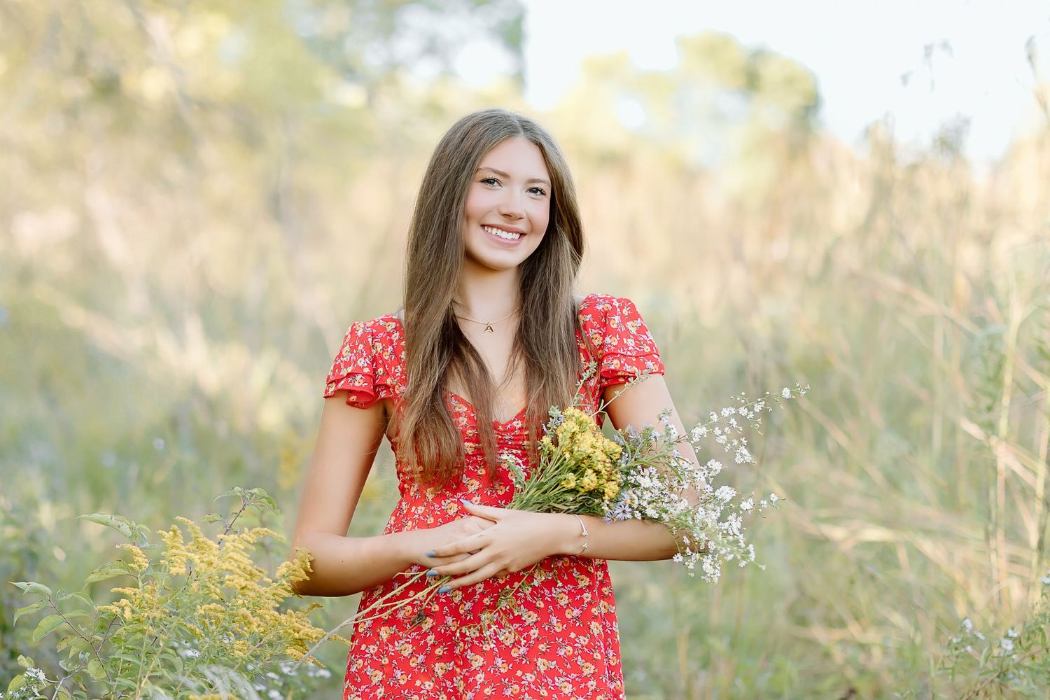 Woman in red polka dot dress poses in sunny field with wildflowers during golden hour photo session.