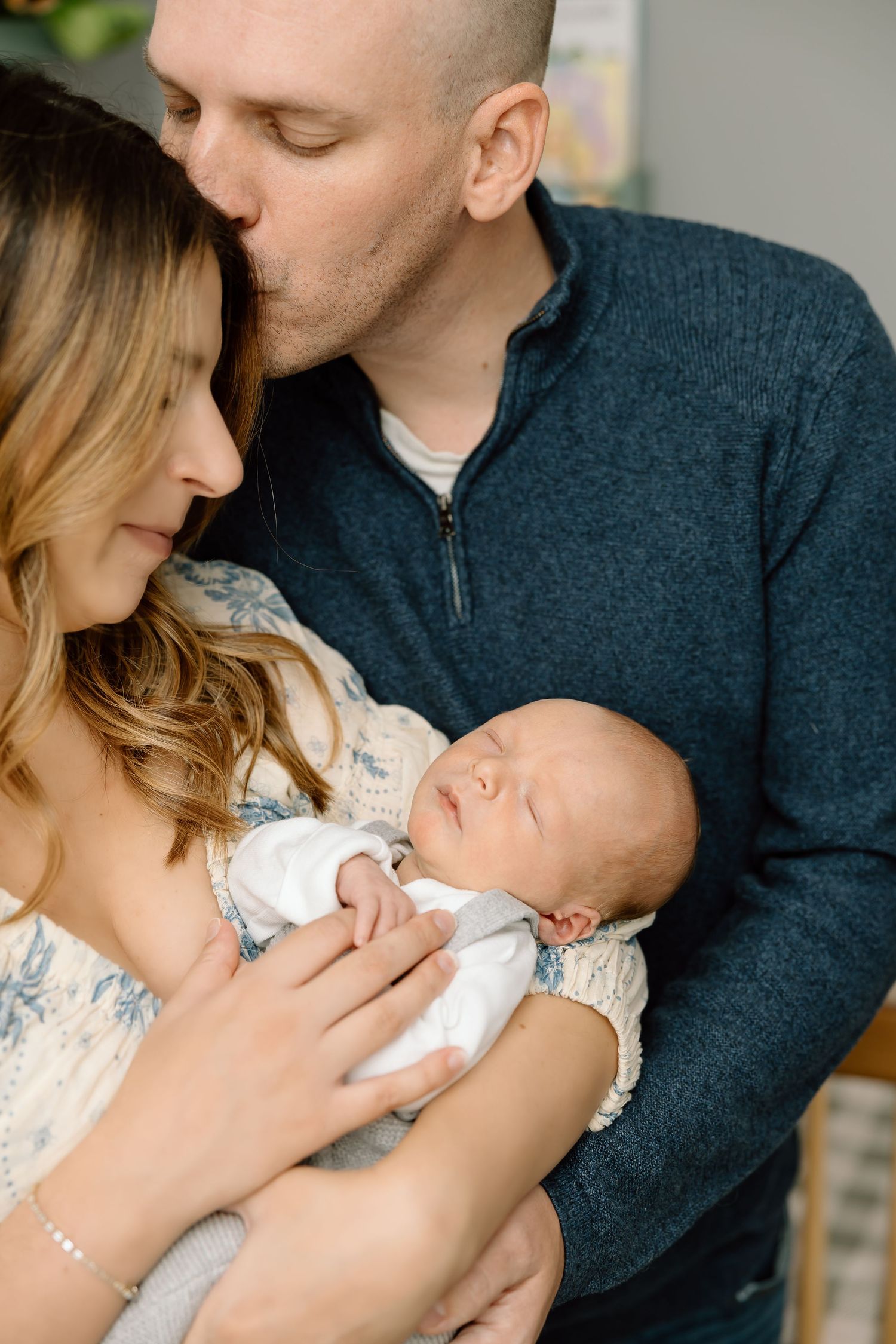 A couple shares an intimate moment while holding their sleeping newborn baby in a tender family portrait.