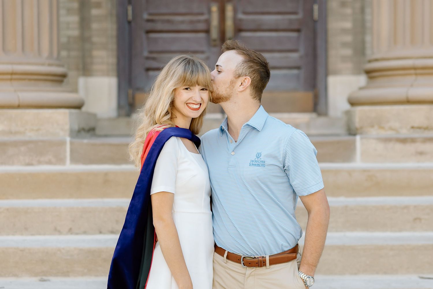 A couple in casual attire shares a romantic moment while standing on stone steps outdoors.