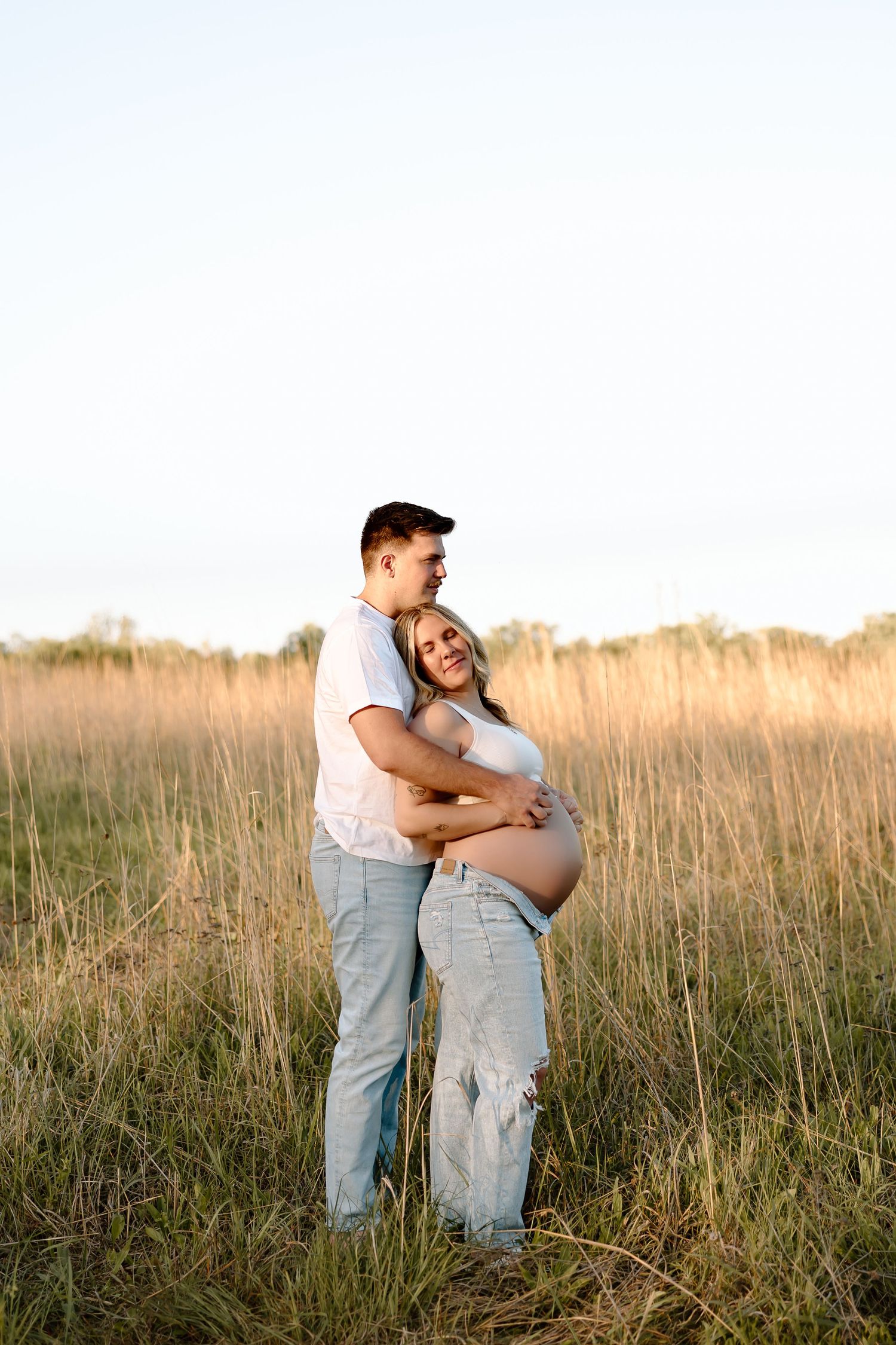 A couple embraces in a golden field of tall grass during sunset, sharing a tender moment together.