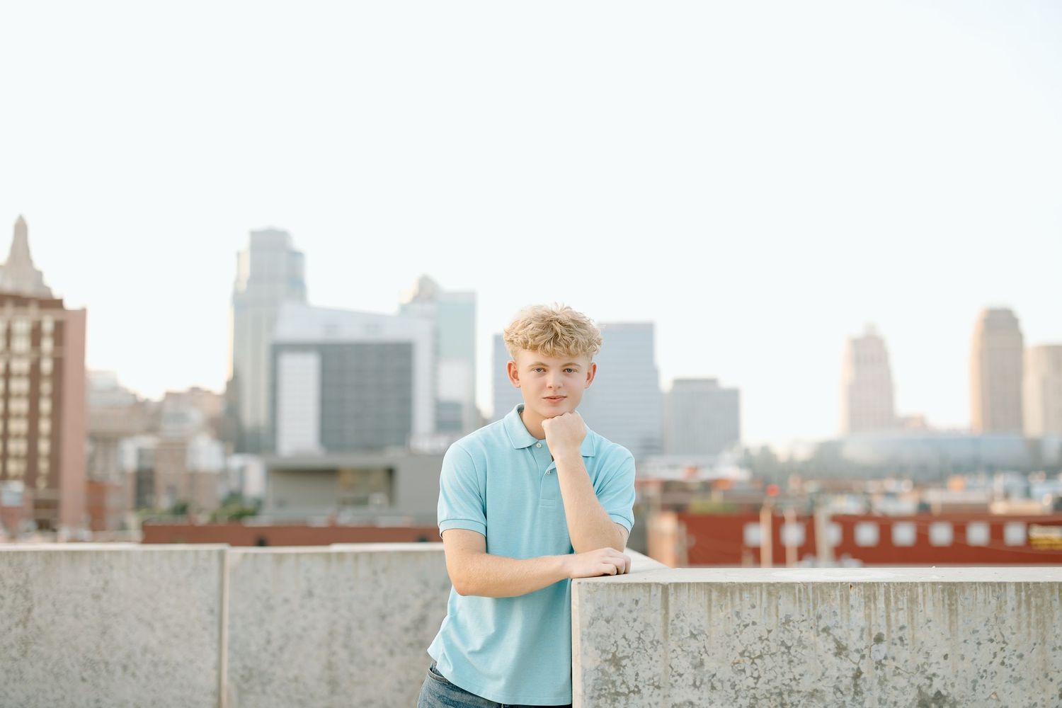 A person in a light blue shirt sits on a rooftop ledge with a city skyline backdrop.