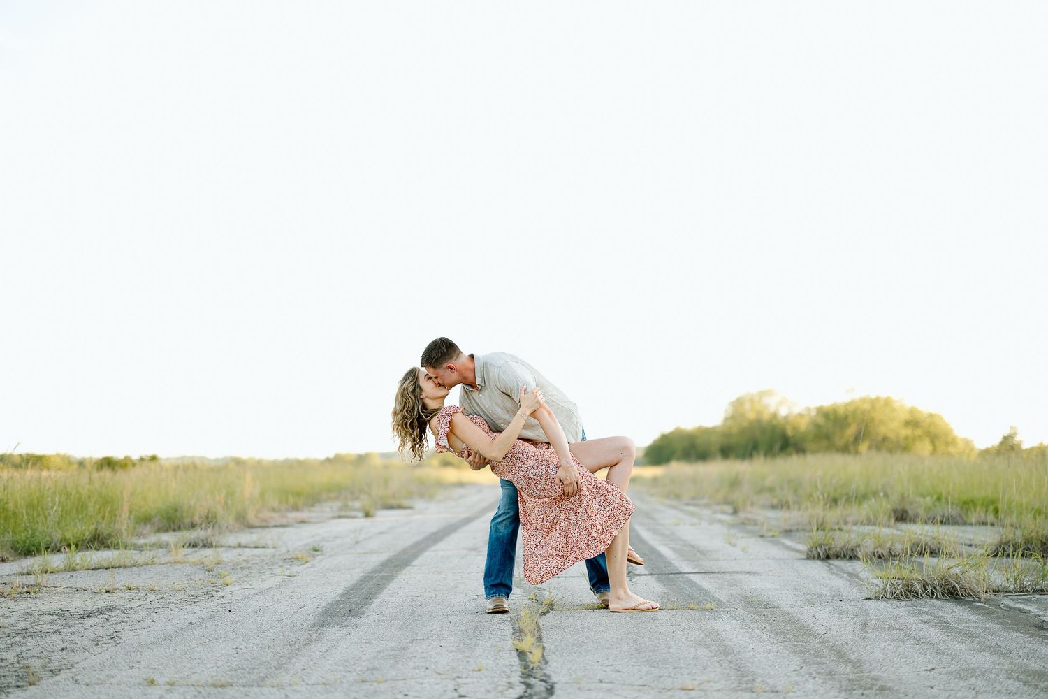 A romantic couple embraces in a dramatic dip pose on a dirt road during golden hour.