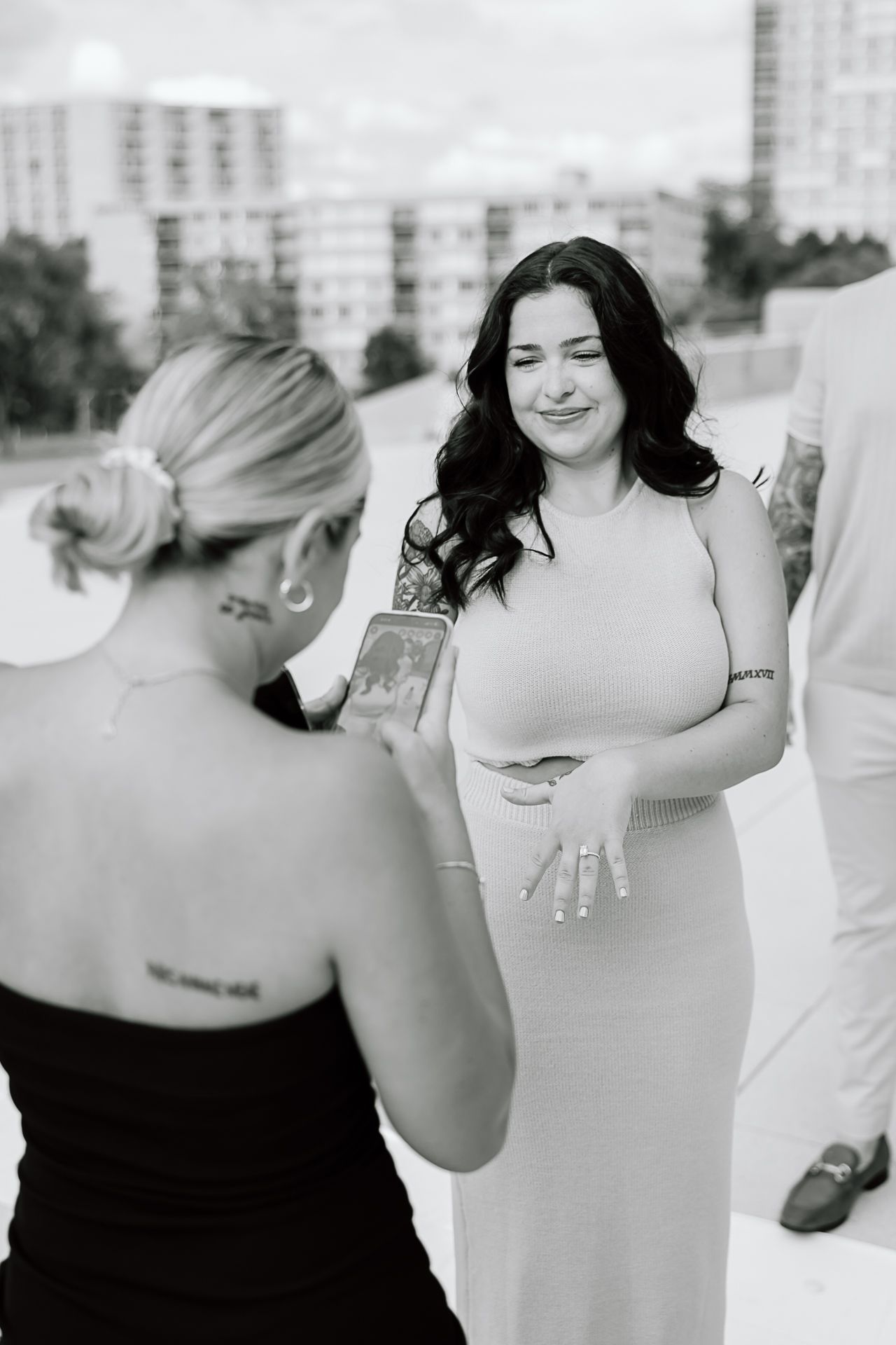 Black and white photo of two people at a formal event sharing drinks and conversation outdoors near city buildings.