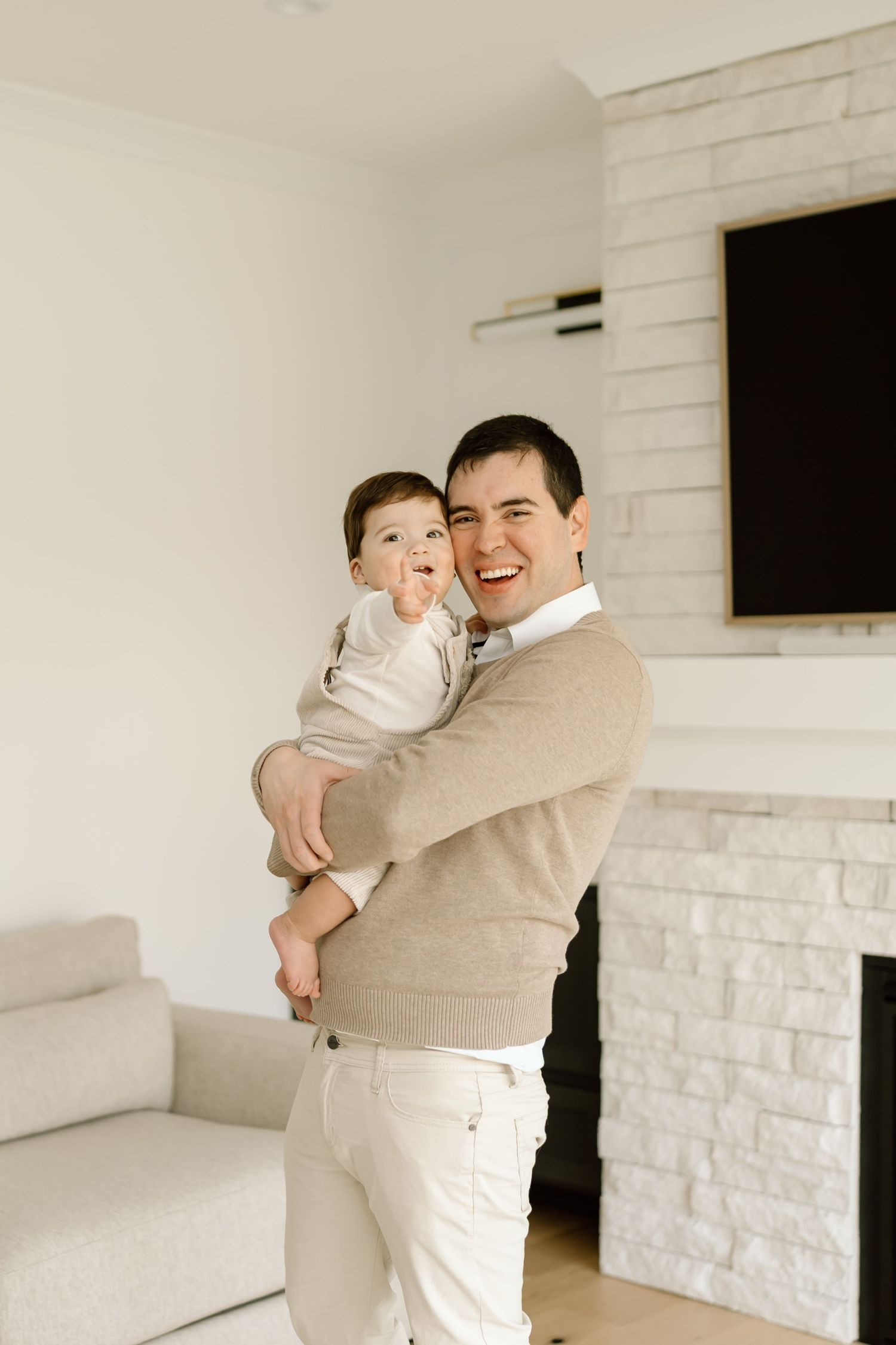 Parent and child share tender moments in white brick room wearing neutral beige and cream colored clothing.