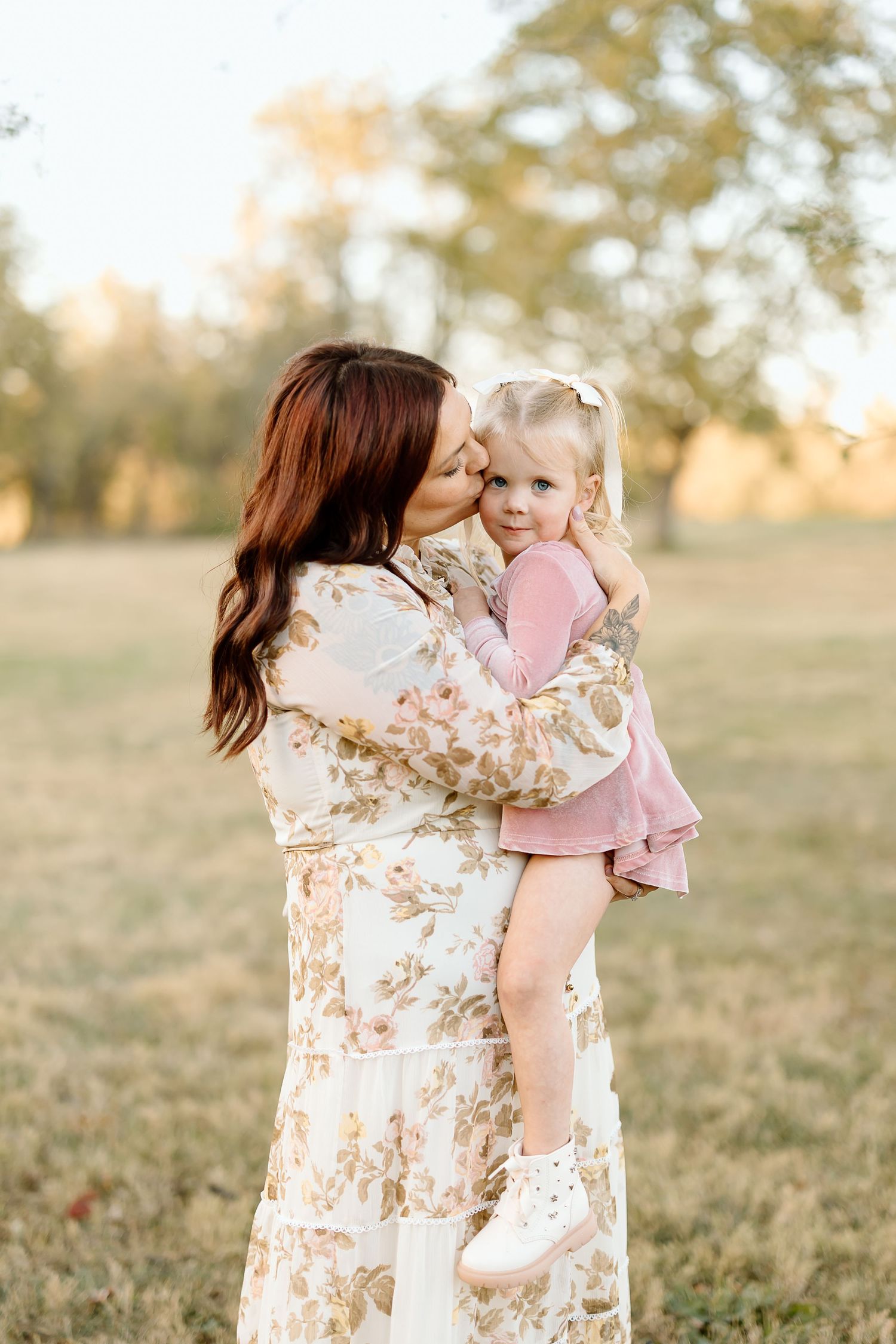 A tender outdoor moment between parent and child wearing pink and floral dress during golden hour in a grassy field.