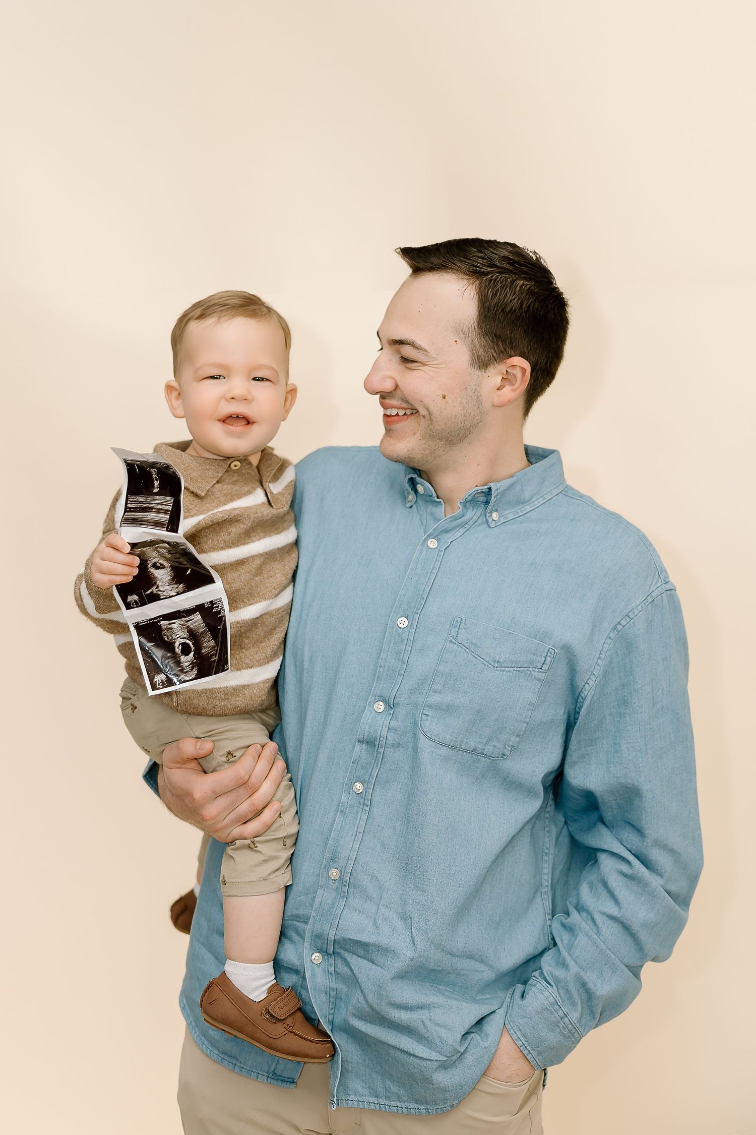A parent in a blue button-down shirt holds a small child who is playing with a vintage camera.