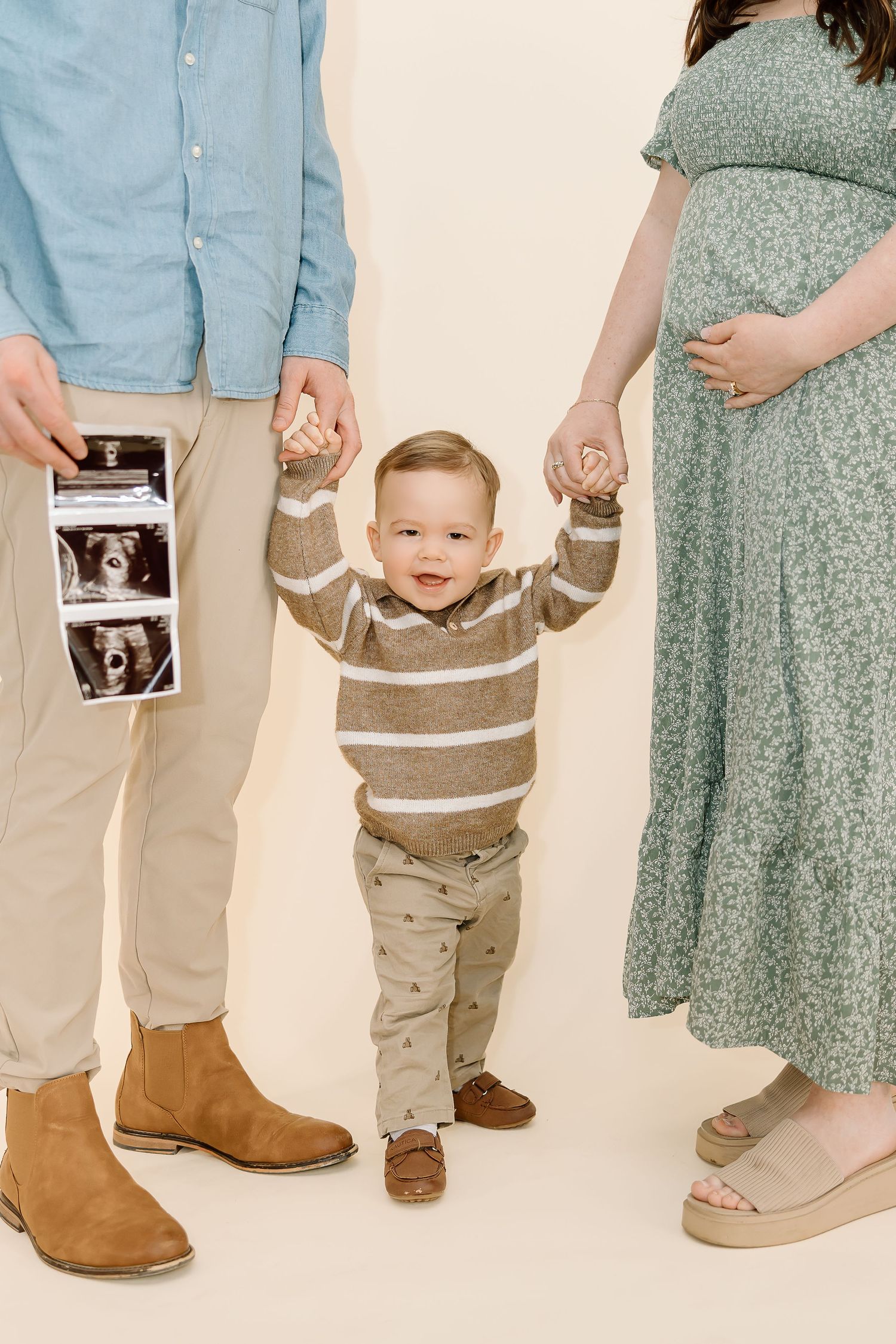 A creative pregnancy announcement photo series showing a toddler in brown sweater holding ultrasound photos with family.