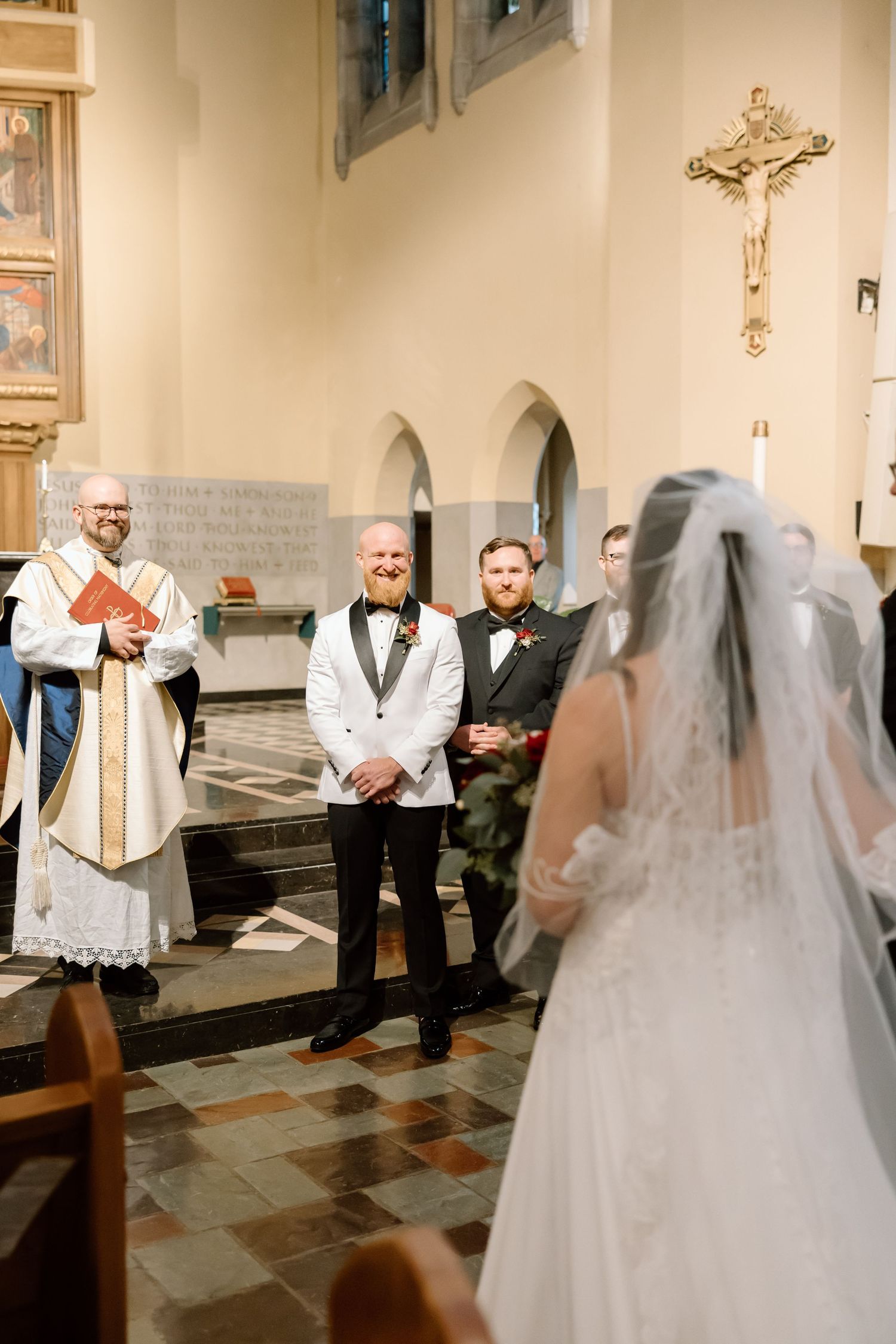A traditional Catholic wedding ceremony takes place inside a church with ornate decorations and a crucifix on the wall.