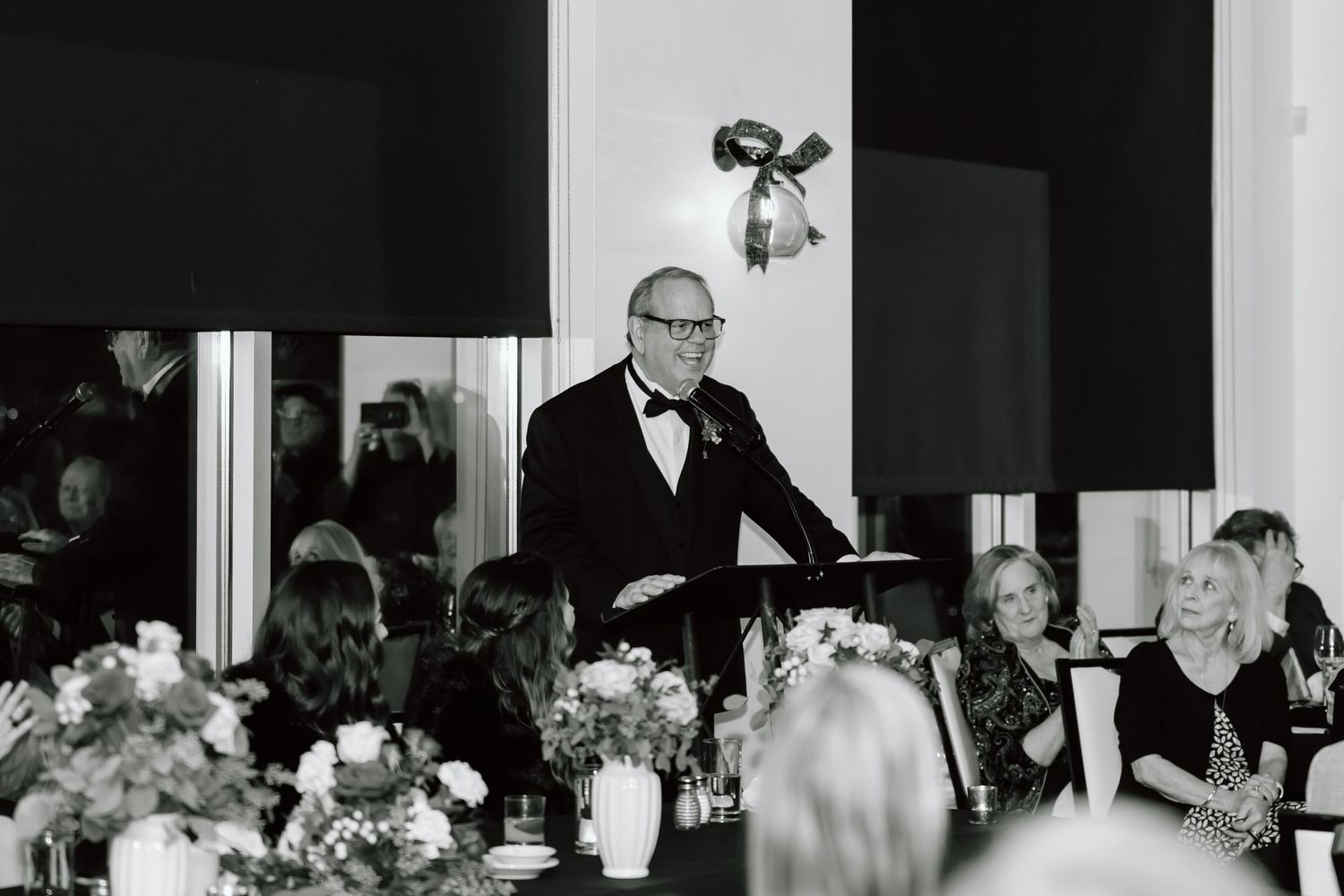 A black and white photograph showing a formal wedding reception with tables, guests, and decorative floral arrangements.