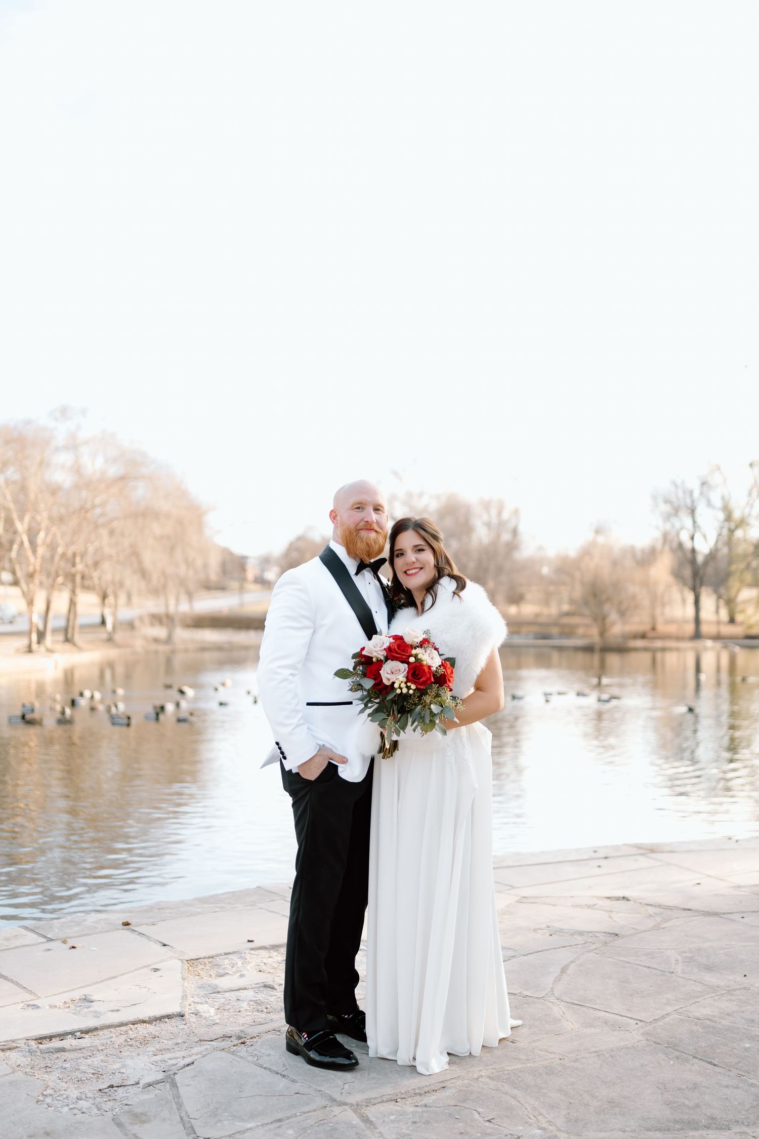 A romantic winter wedding photo session by a lake with a couple in formal attire sharing intimate moments.