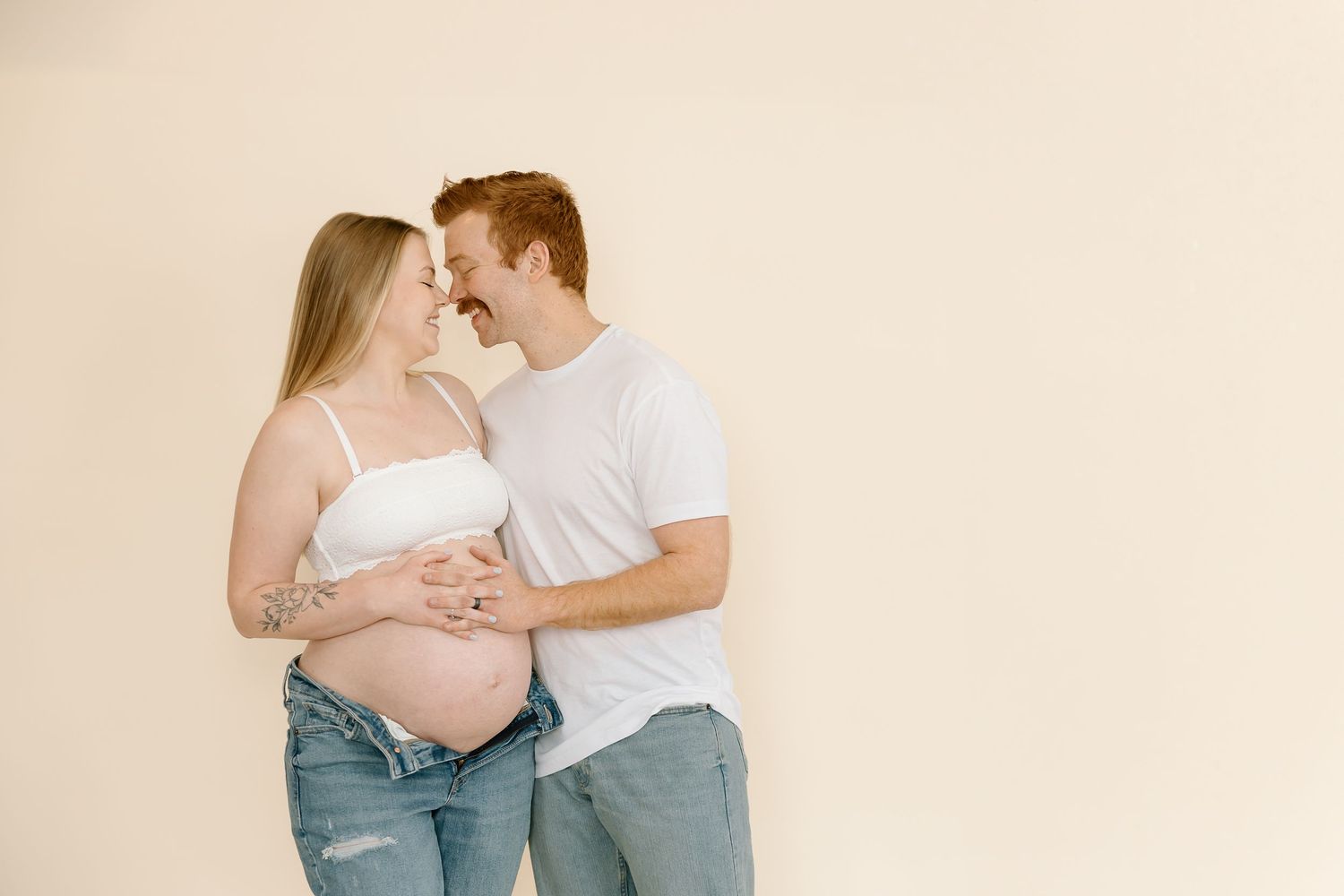 Intimate maternity portrait of couple sharing loving moment against neutral background.