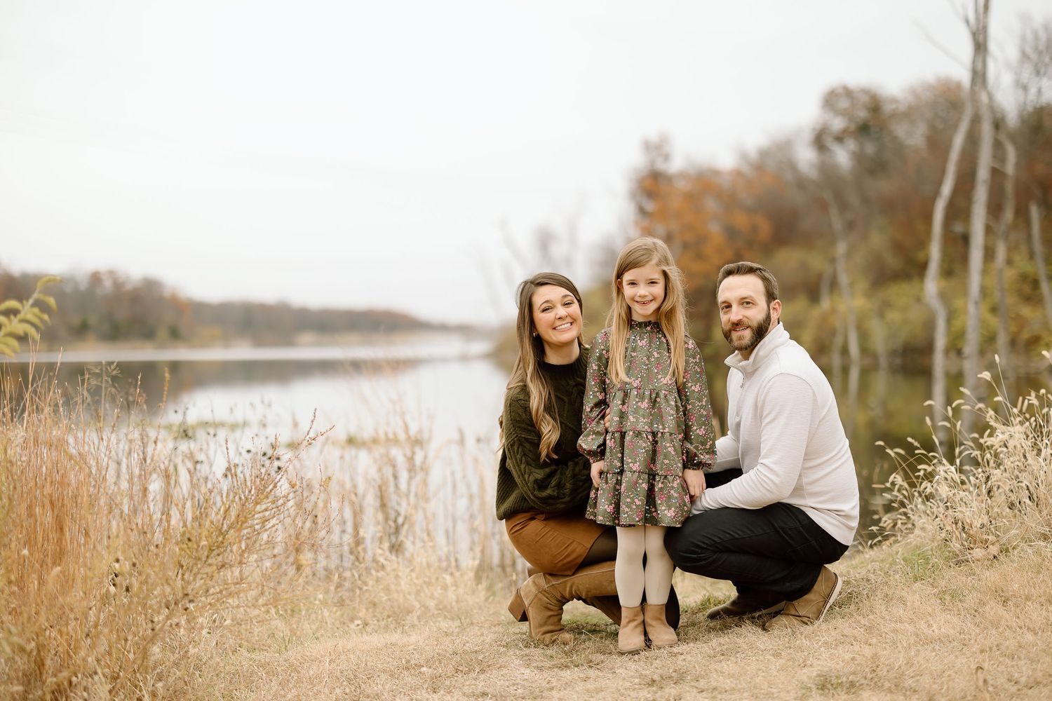 Family kneeling together for a casual portrait by the lake during fall.