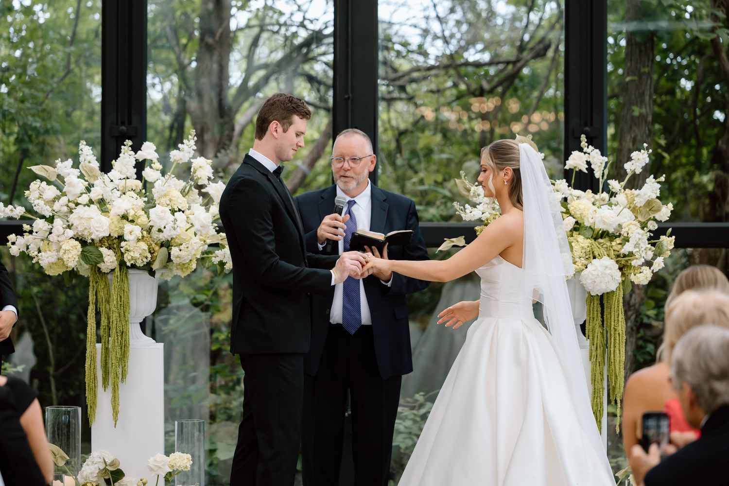 Bride and groom exchanging vows at elegant indoor wedding ceremony with white floral arrangements.