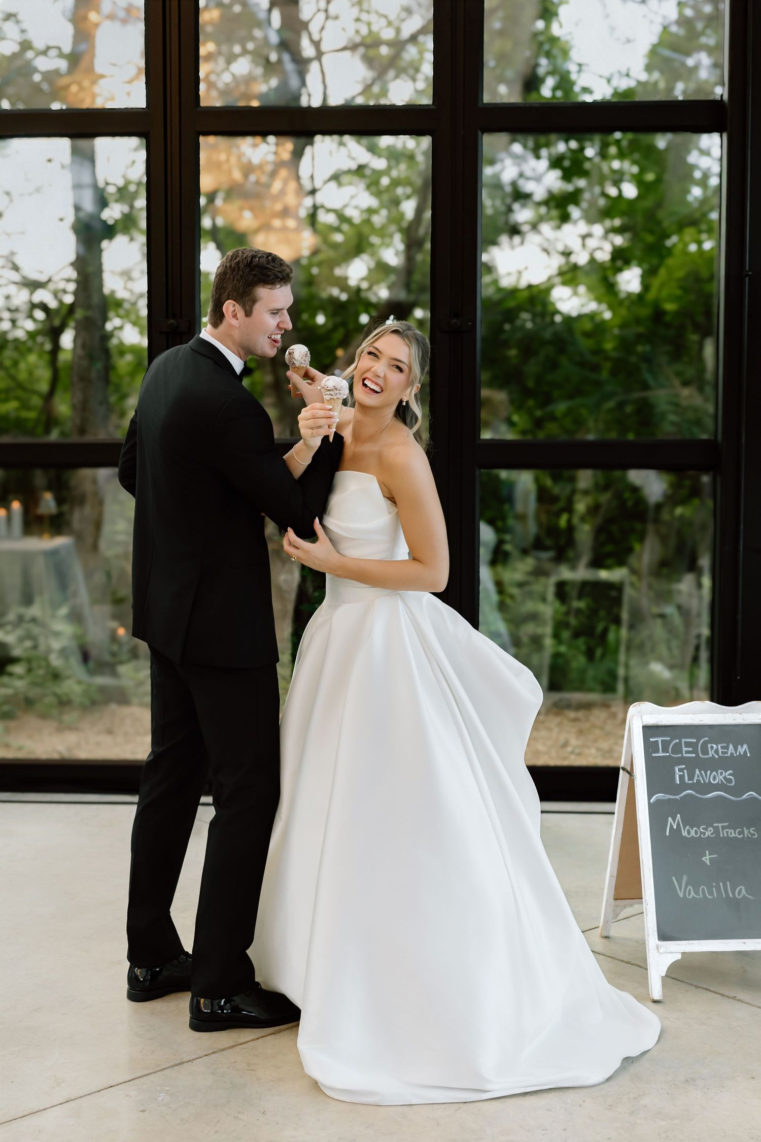 Bride and groom sharing a joyful moment at their wedding reception near an ice cream flavor chalkboard sign.
