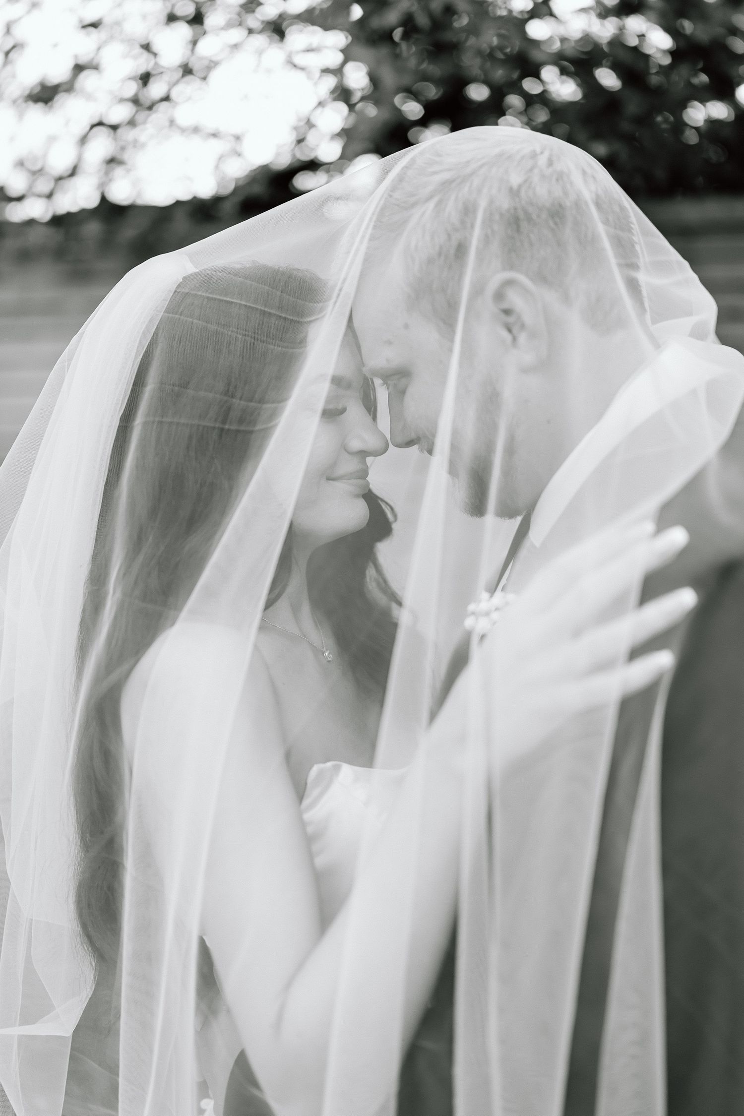 A romantic black and white wedding photo of a couple sharing an intimate moment under a delicate veil.