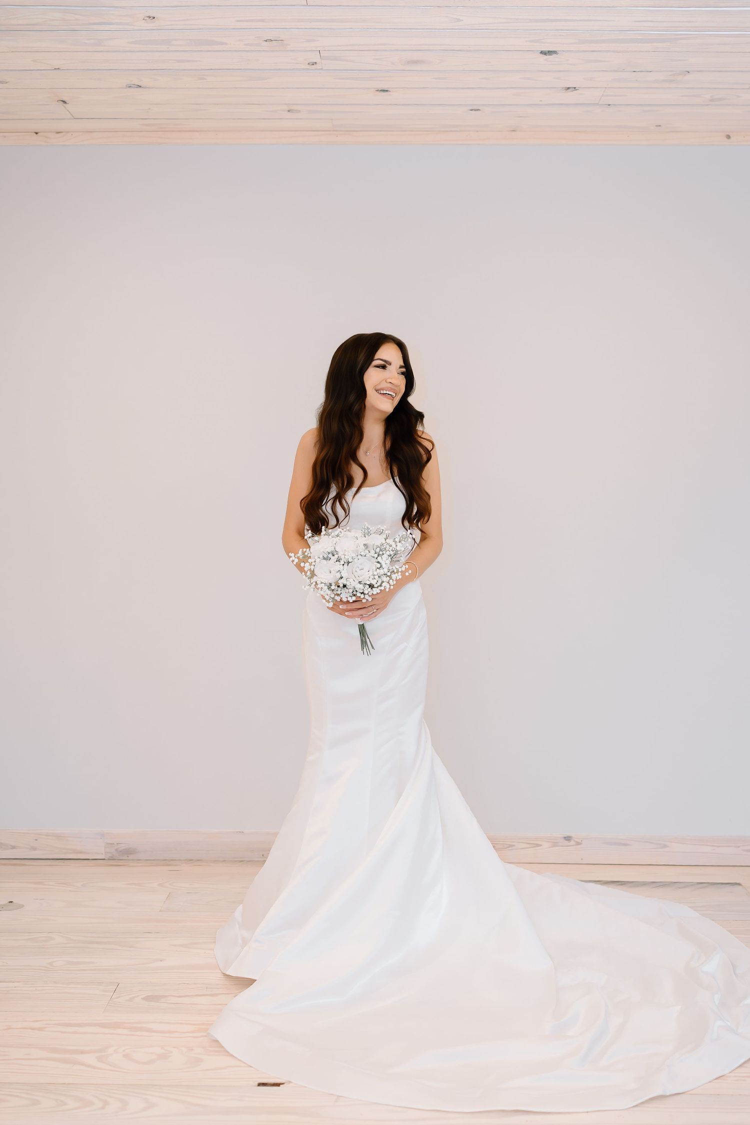 A bride in a flowing white wedding gown poses gracefully in a studio setting against a light backdrop.