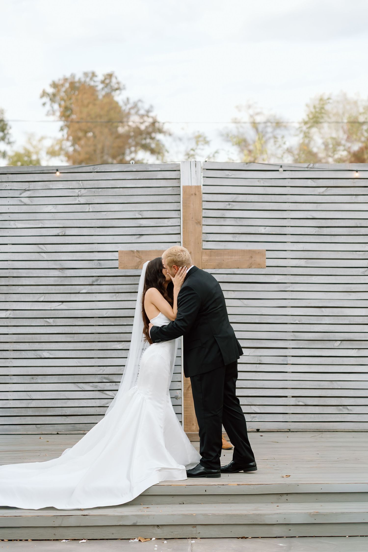 A couple shares a romantic moment in front of a wooden cross during their outdoor wedding ceremony.