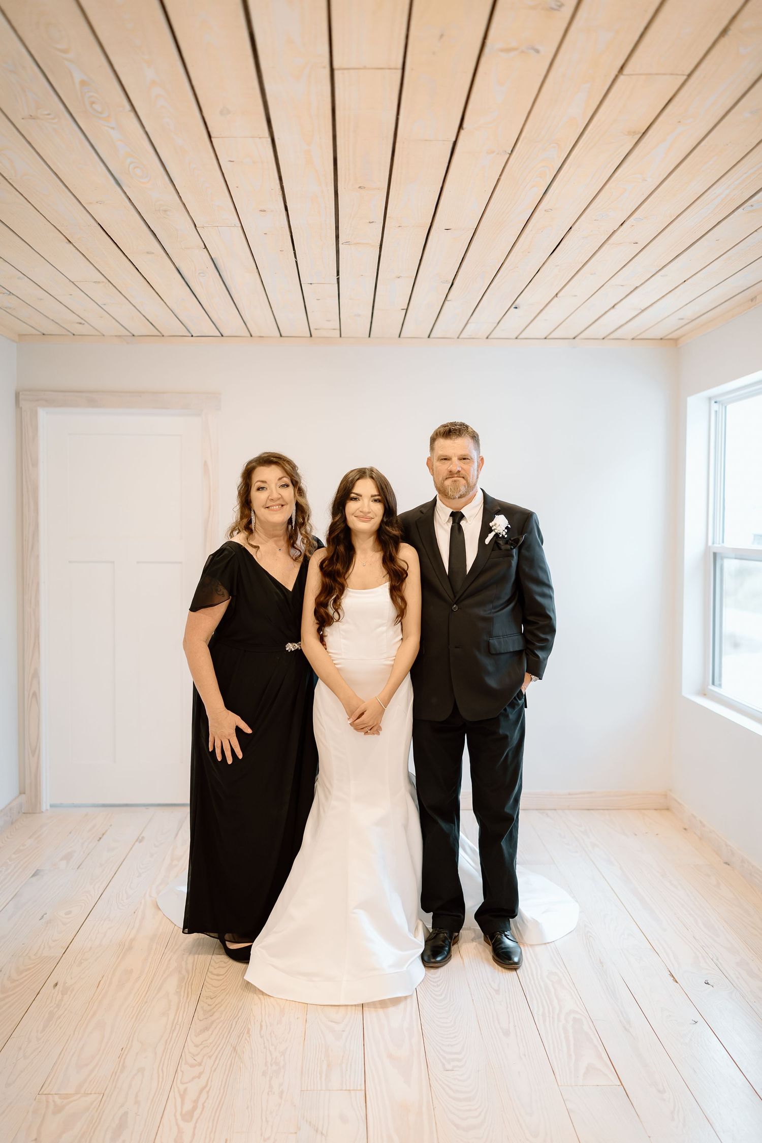 Wedding party poses creatively in a bright white room with wooden floors and paneled ceiling.