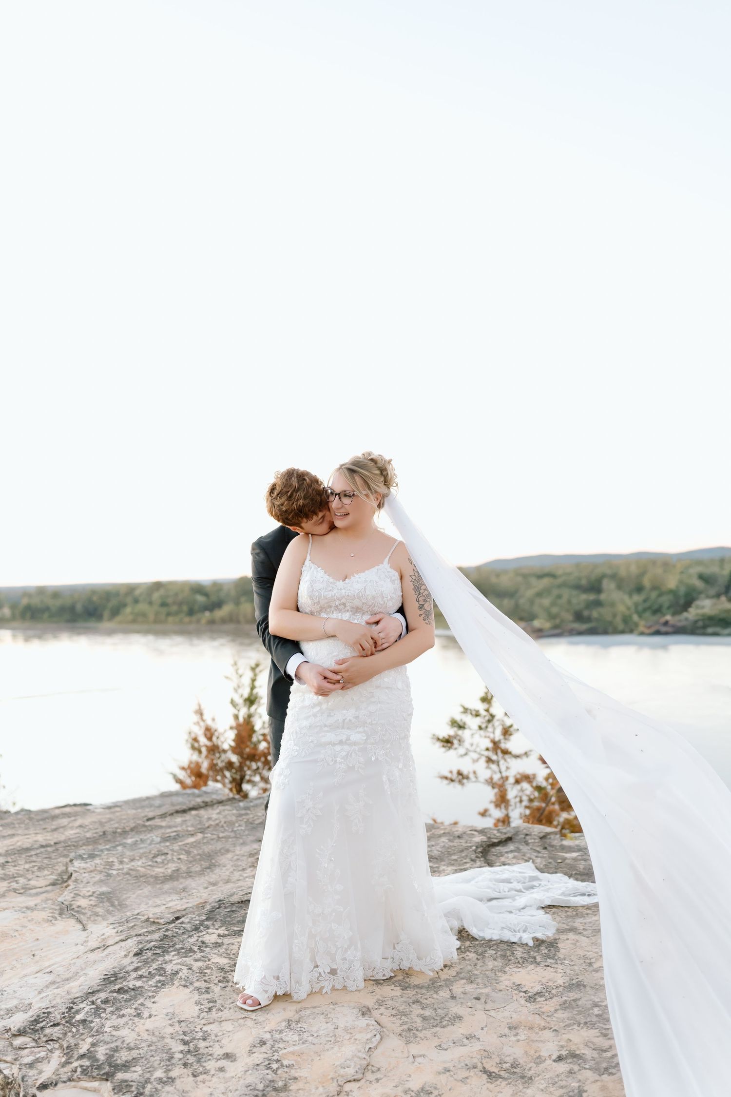A romantic beach wedding scene with a flowing white veil blowing in the wind by the water's edge.