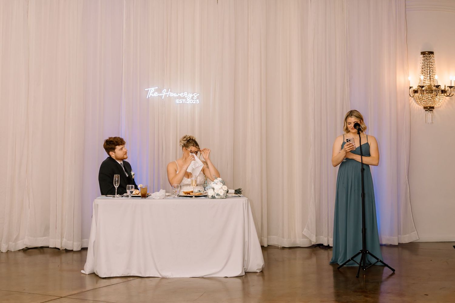 A wedding reception hall decorated with white drapes features elegant table settings and chairs in teal blue.