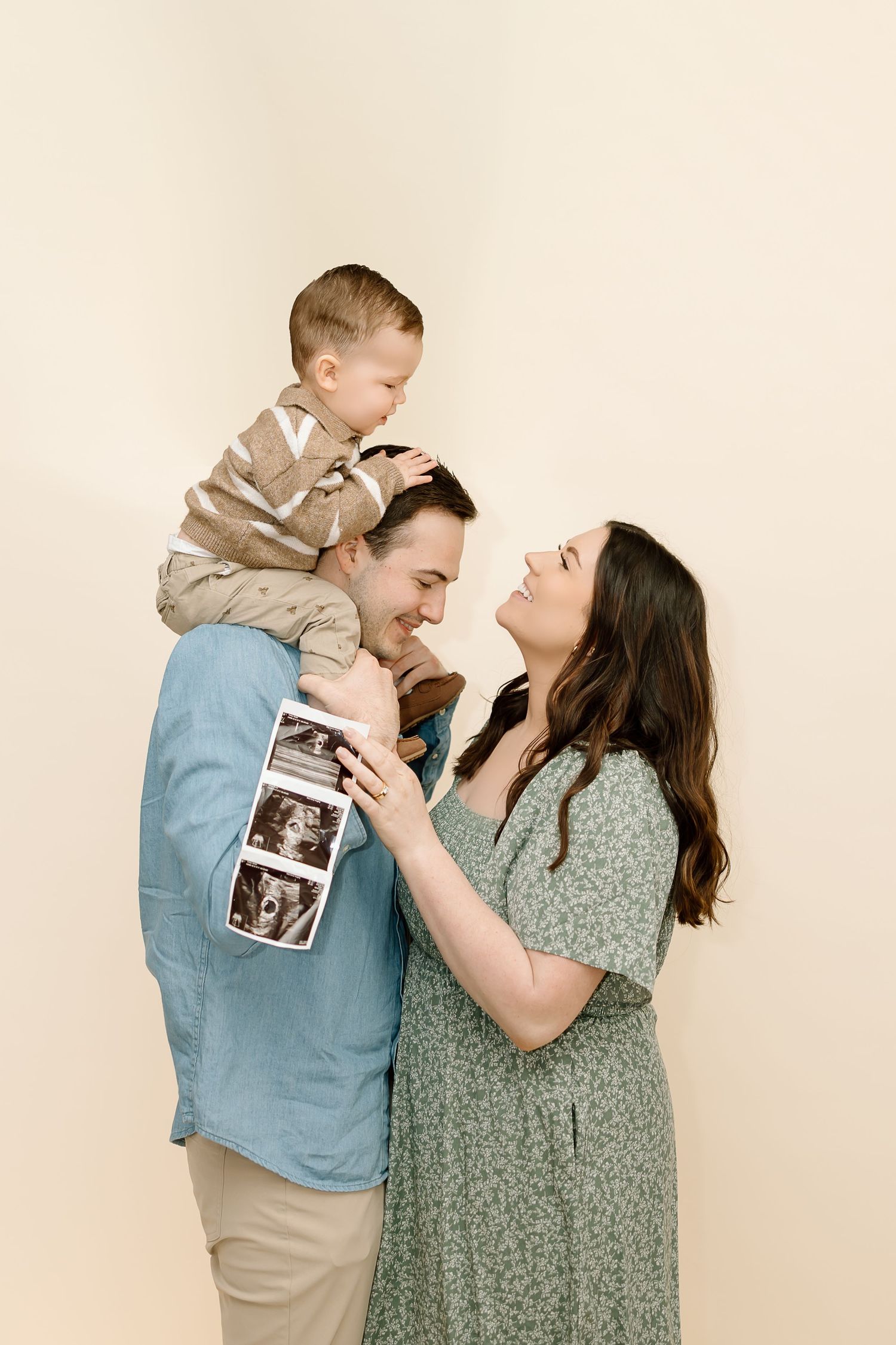 A family shares joyful moments in a series of cream-colored studio photos while holding an ultrasound image.