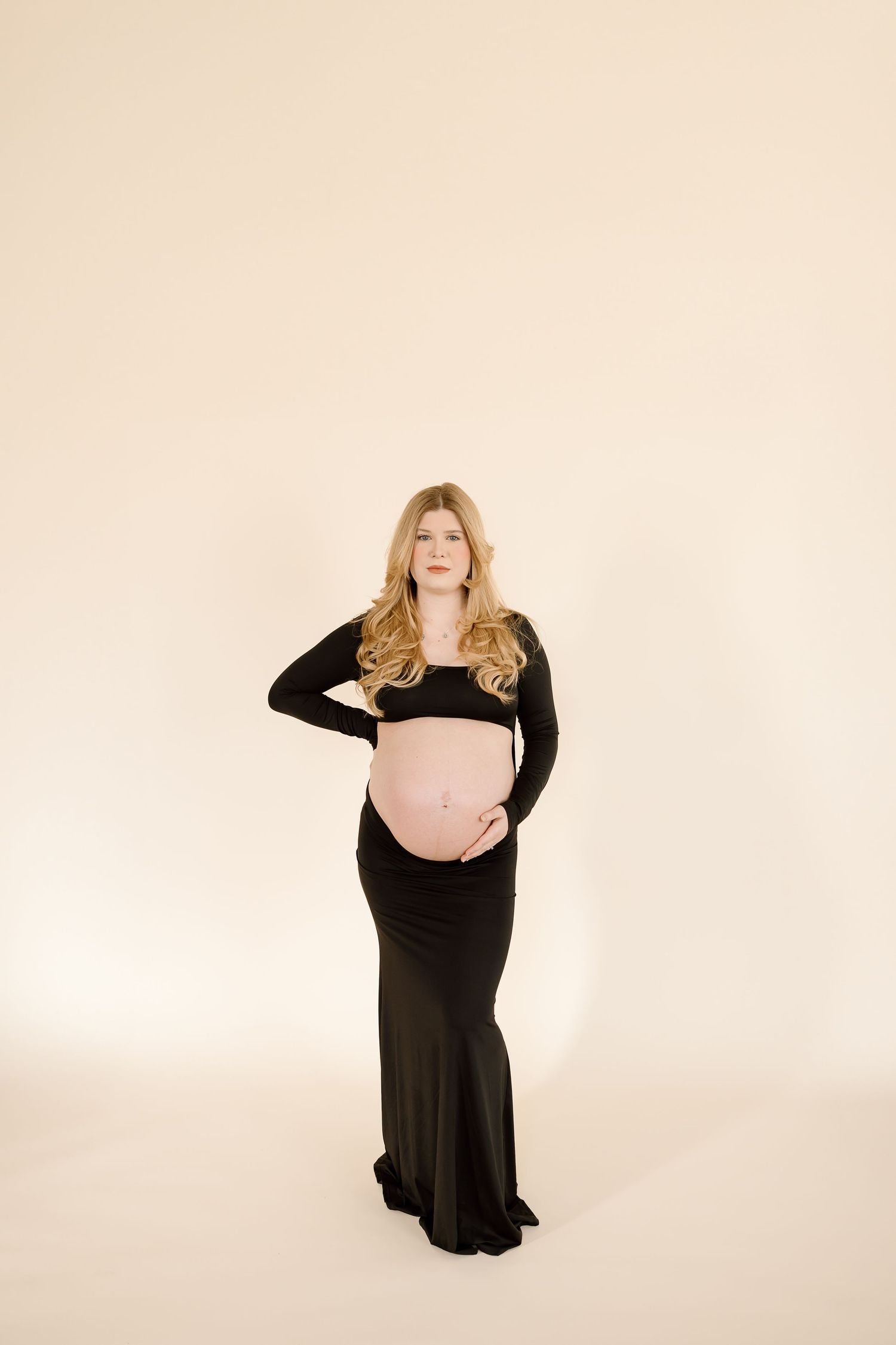 A maternity photo series showing a woman in a black dress against a cream background in different poses.