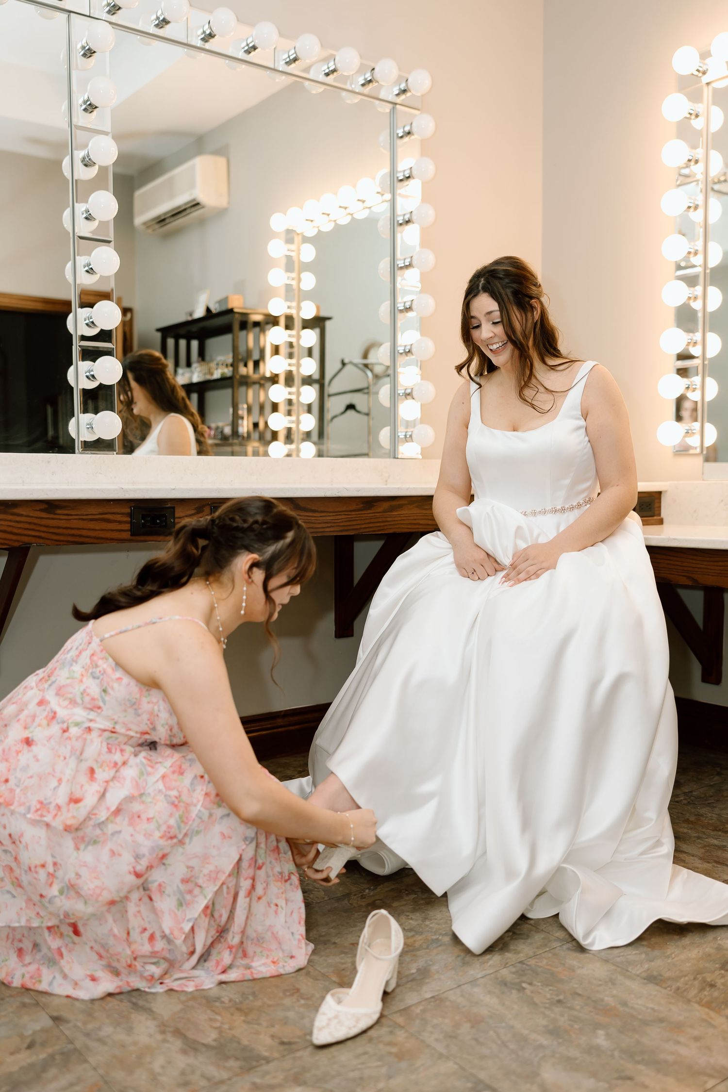 A series of images showing someone in a pink floral dress helping adjust a white wedding gown in a dressing room with mirrors.