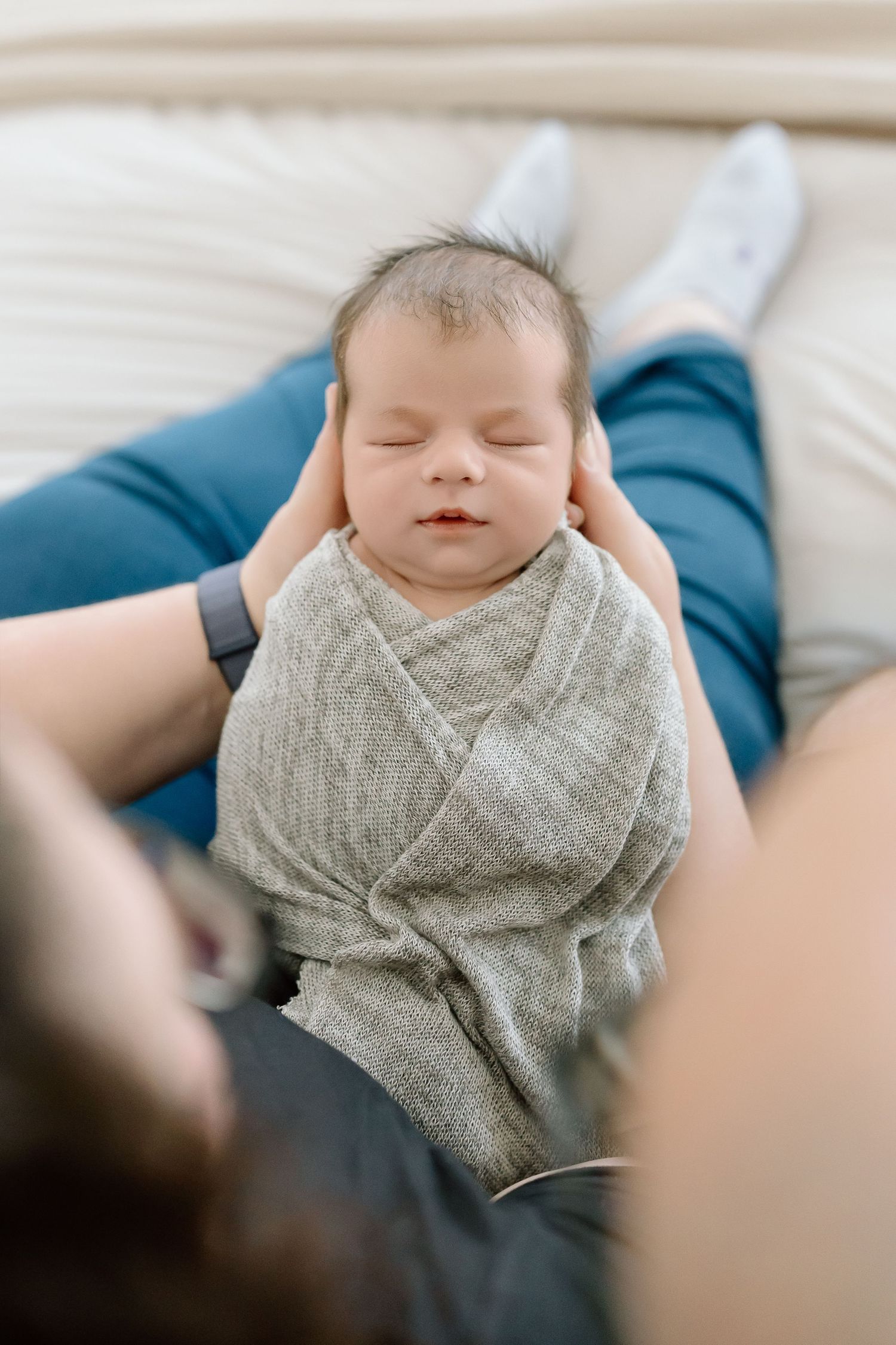 A sleeping baby wearing a soft gray wrap lies peacefully on a light-colored surface.
