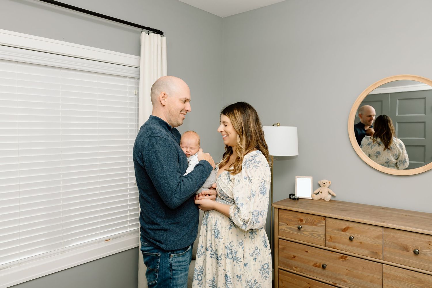 People interact in a modern nursery room with wooden furniture and gray walls.
