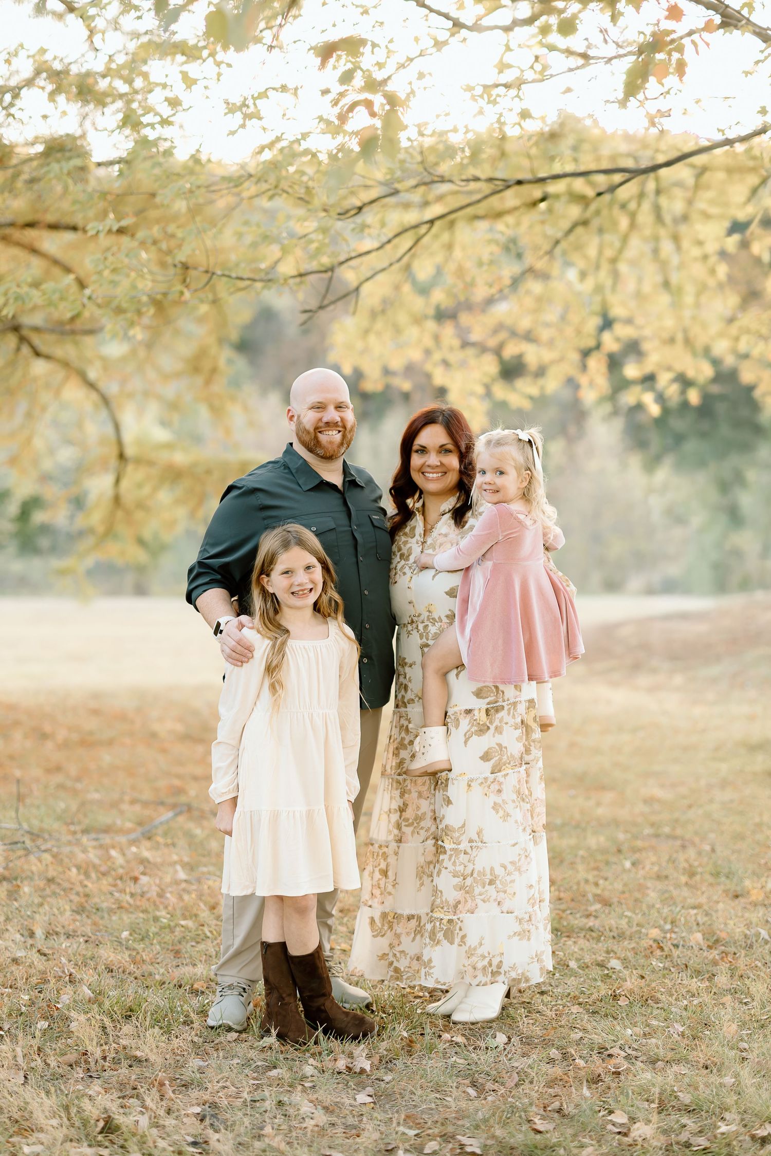 A family stands together outdoors in autumn with golden leaves and sunlight creating a warm, ethereal atmosphere.