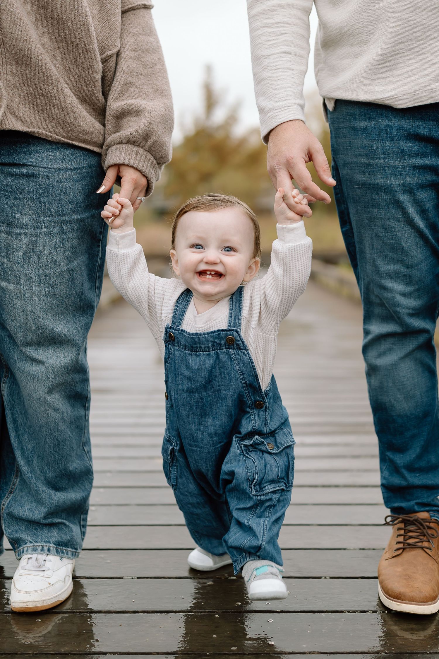 A sequence of feet showing a toddler walking while holding hands with an adult on a wooden deck.