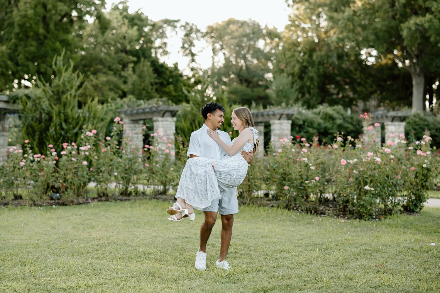 A couple embraces in a romantic moment while standing in a lush garden setting with blooming flowers and greenery.