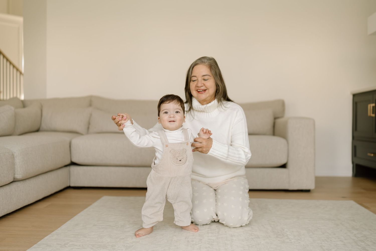 Two young children in white pajamas play and laugh together on a light colored couch.