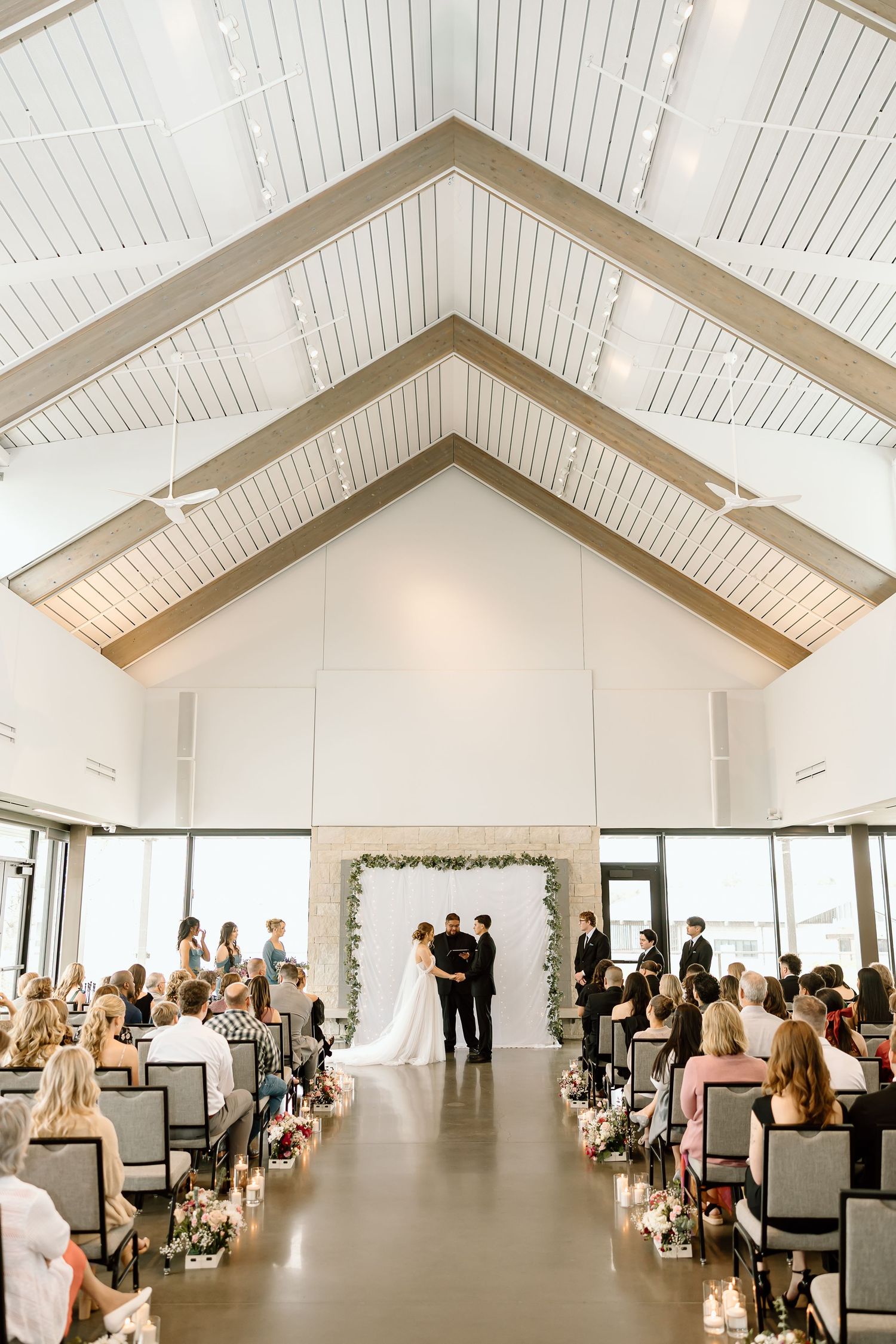 Modern wedding venue with vaulted white ceiling and rows of chairs leading to floral arch.