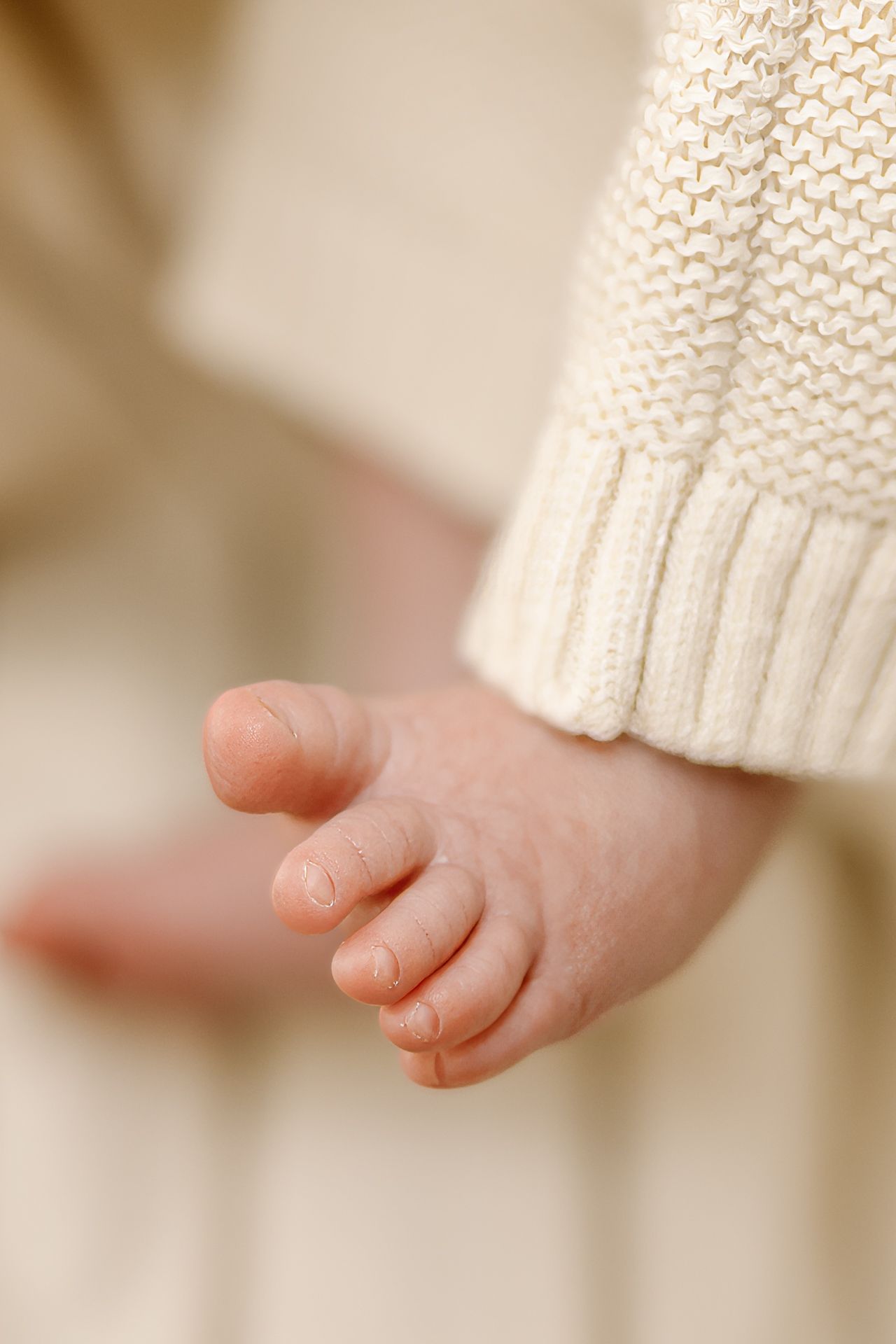 Close-up of tiny baby toes peeking out from beneath a white knit sweater sleeve.