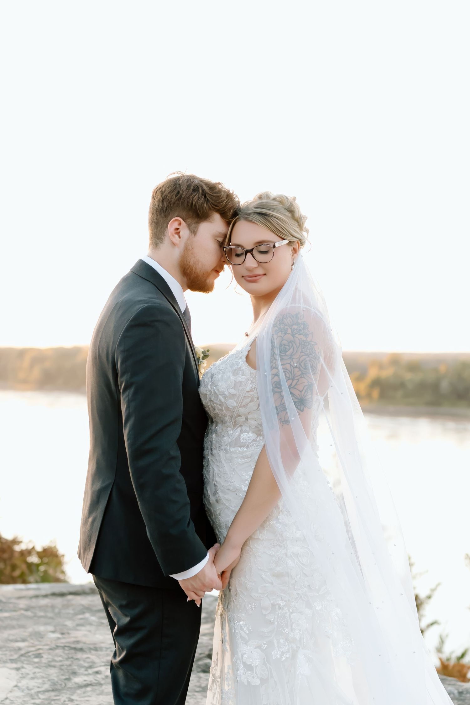 A romantic wedding couple shares intimate moments by a serene lakeside at sunset.