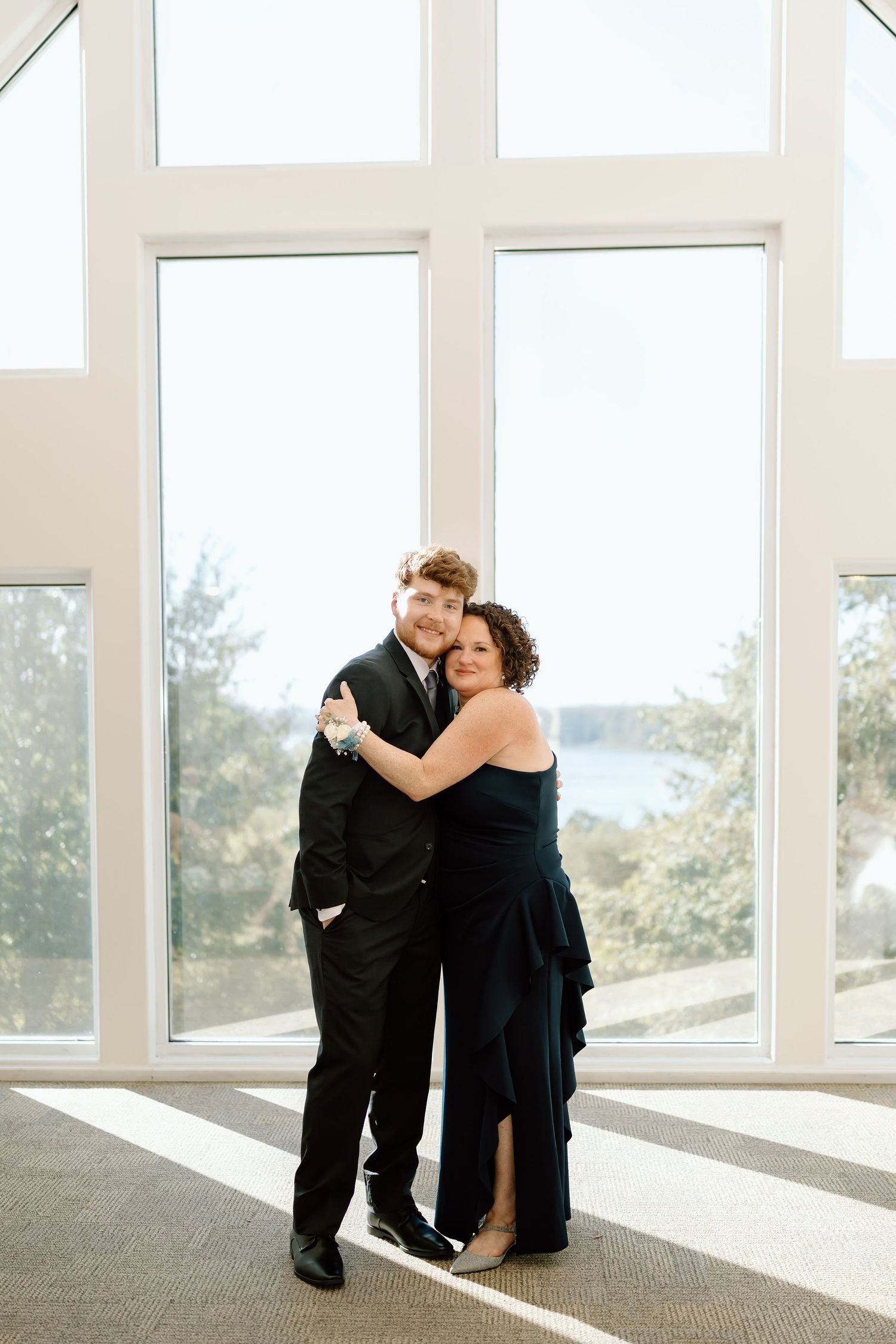 A couple shares an intimate dance in a bright sunlit room with floor-to-ceiling windows.