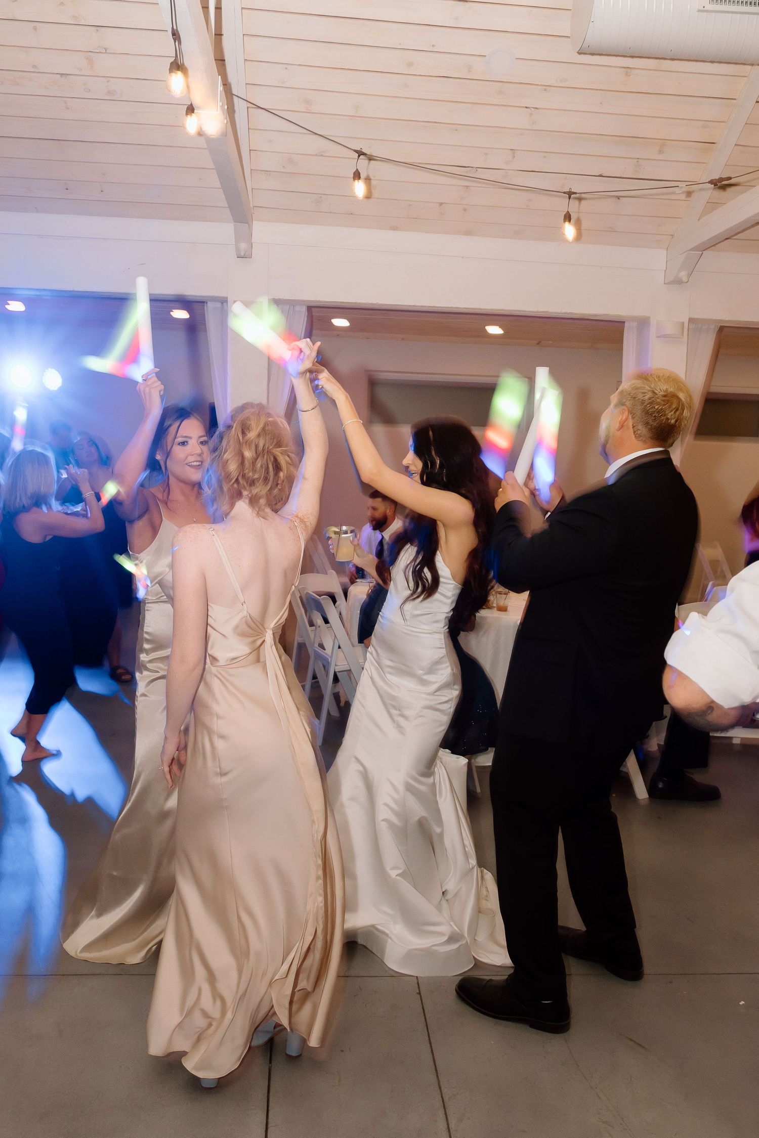 Wedding guests dancing together in a line at a reception venue with white walls and track lighting.