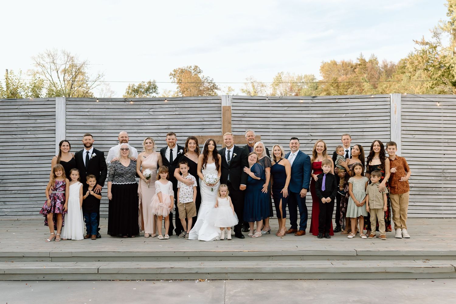 Wedding party members stand in a line on gray steps for a series of formal group photos outdoors.