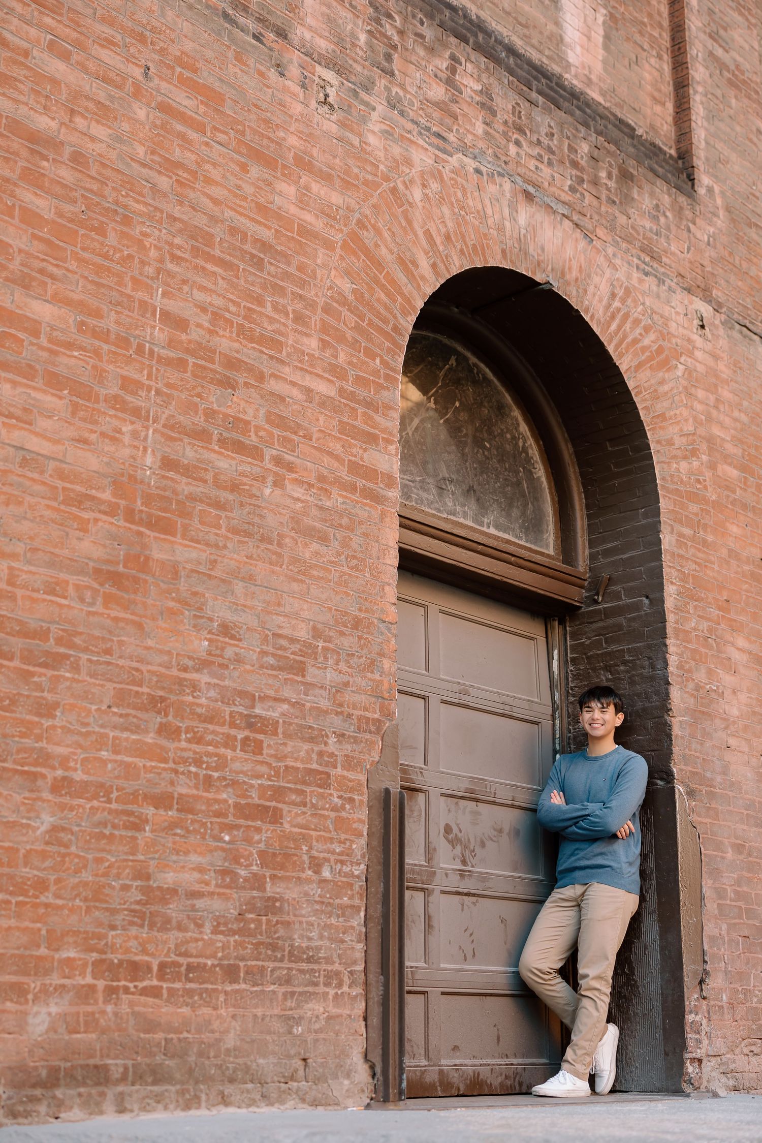 Person posing in blue sweater against vintage arched doorway and brick wall.