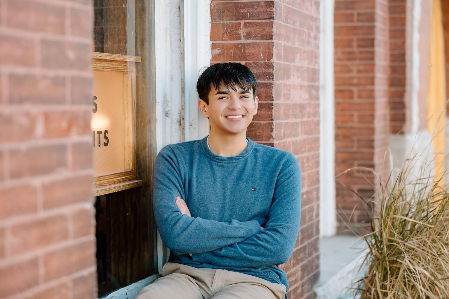 Casual portrait with crossed arms sitting by brick storefront.