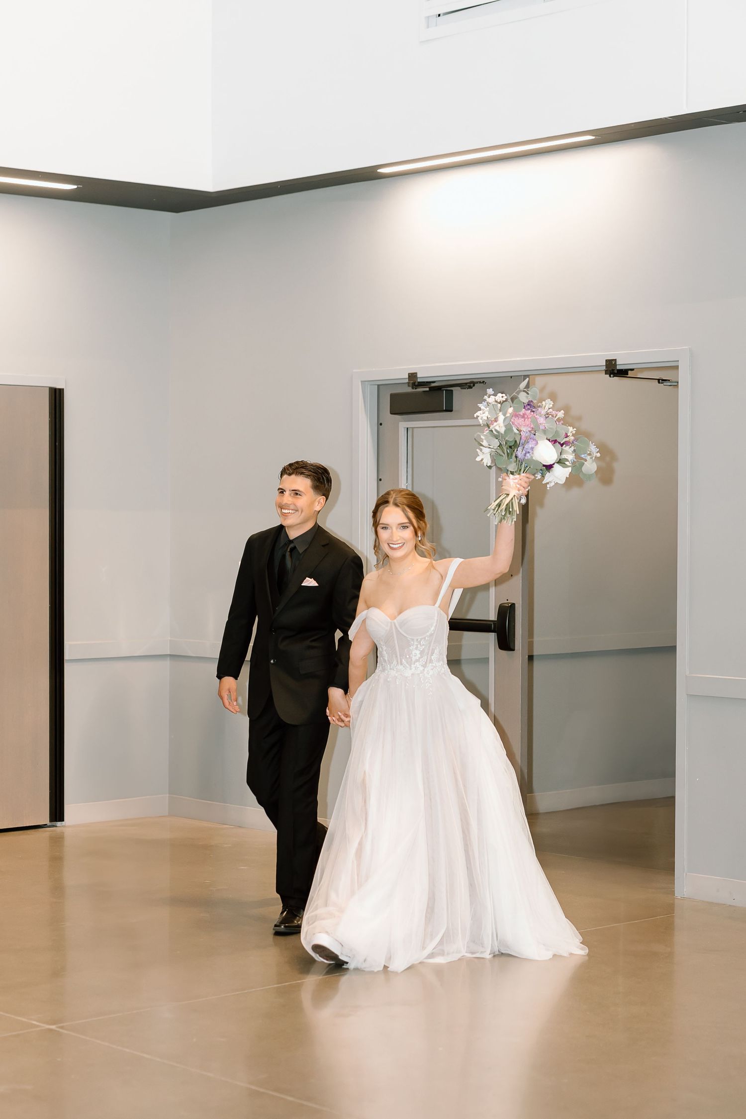 Couple makes grand entrance into reception venue with bride holding floral bouquet.