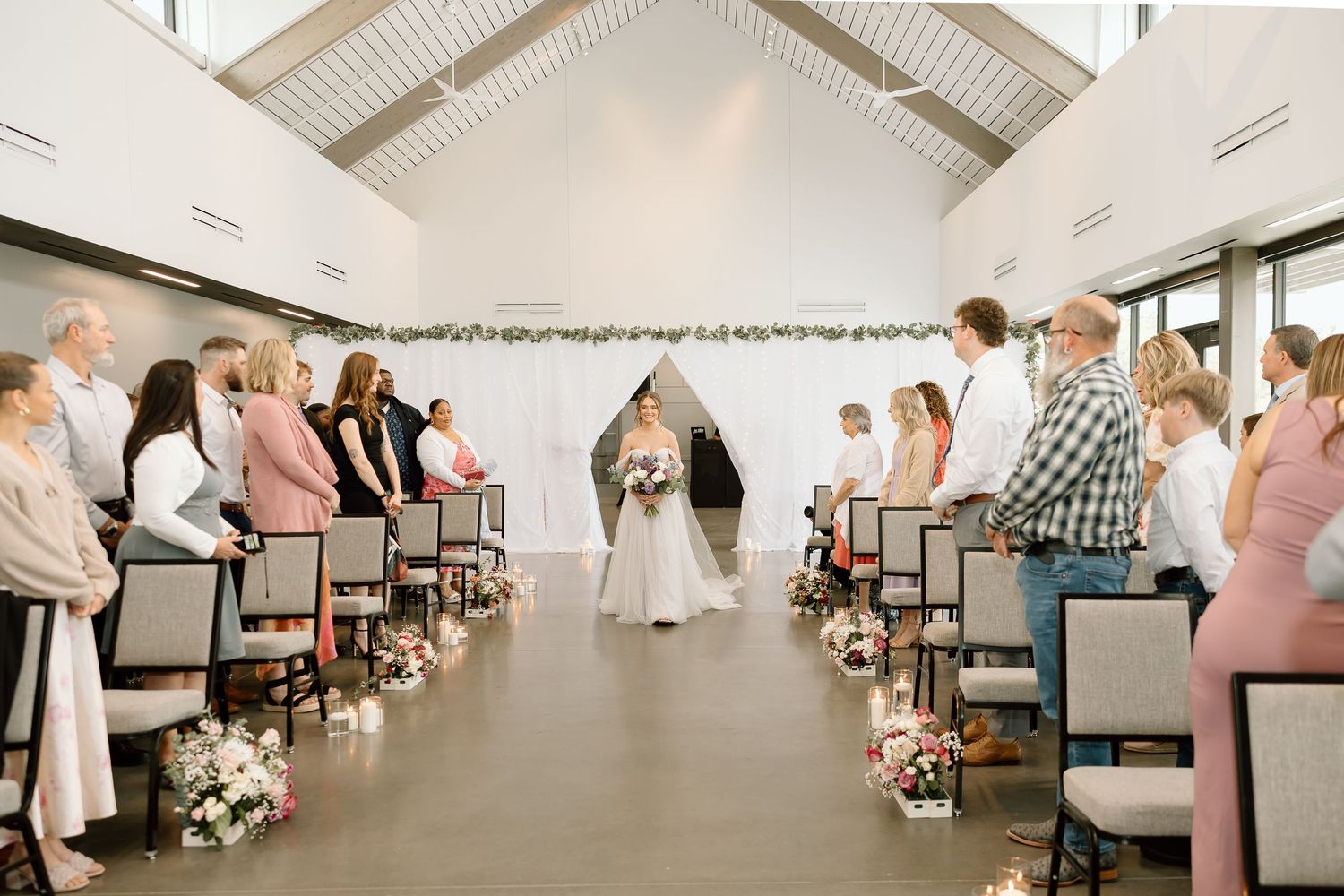Wedding ceremony in modern white chapel with guests seated in rows.